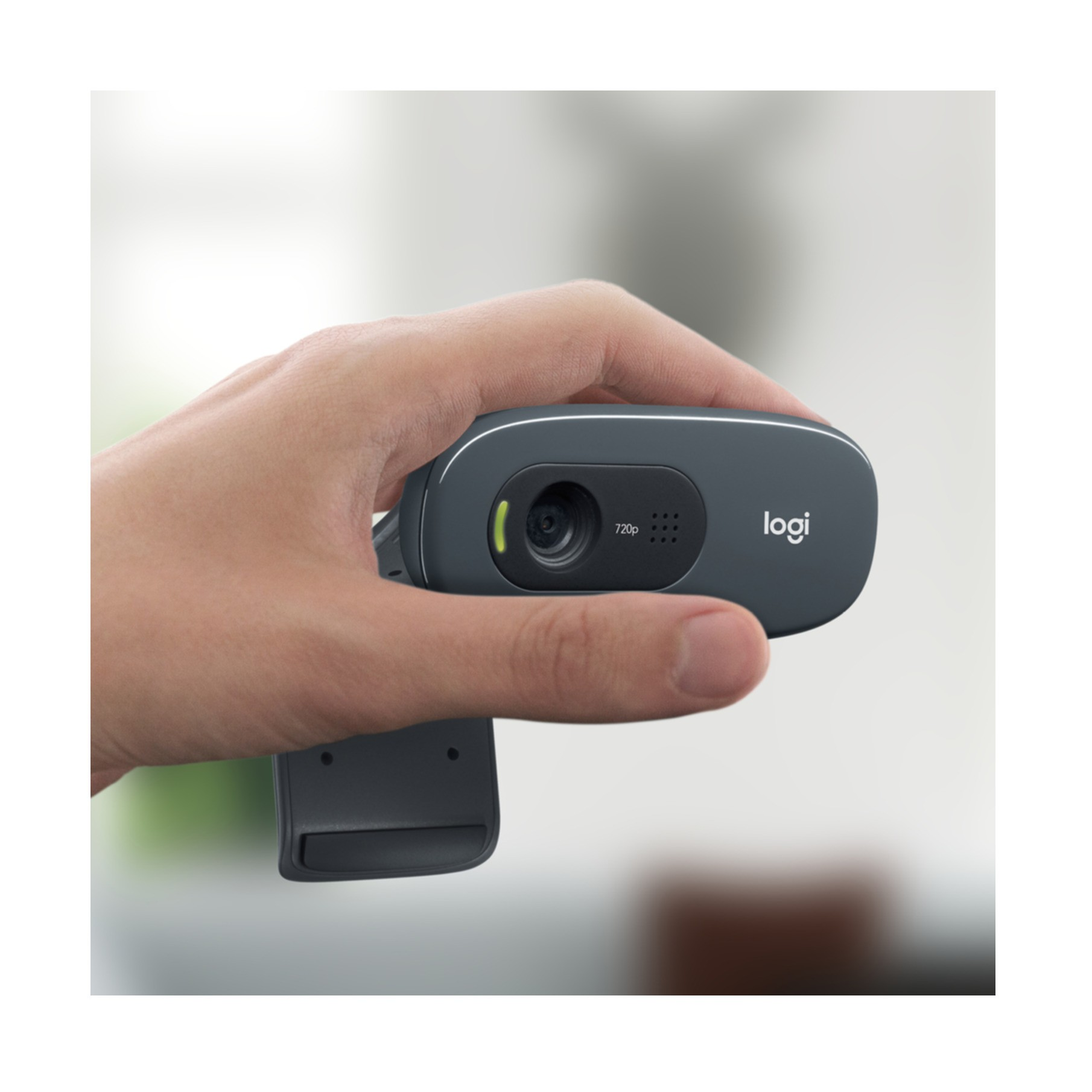 Hand hält eine dunkelgraue Webcam mit Logi-Logo. Der Hintergrund ist unscharf.