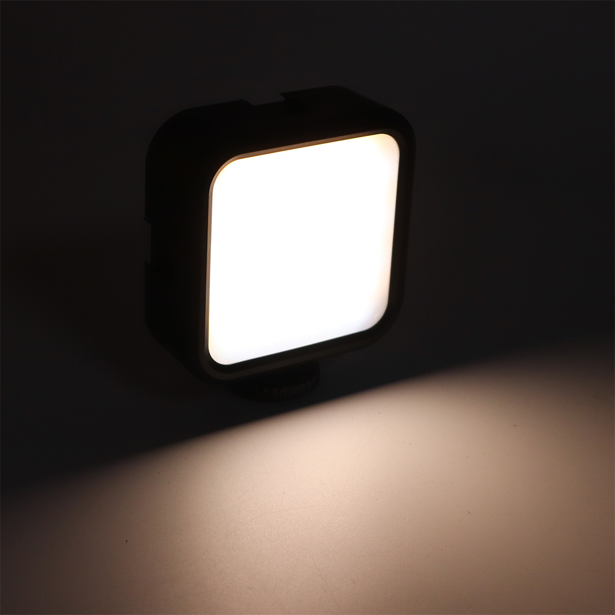Ein kleines, quadratisches, schwarzes LED-Licht ist eingeschaltet. Es wirft Licht auf eine weiße Oberfläche.