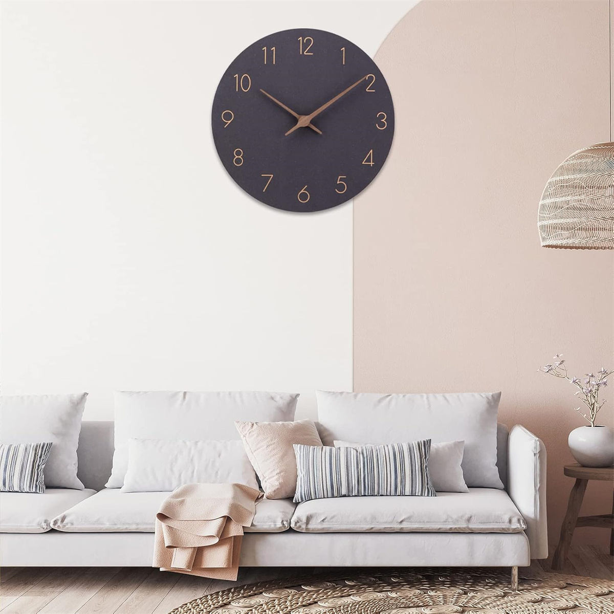 Eine schwarze Wanduhr mit goldenen Ziffern hängt über einem weißen Sofa. Die Wand ist zweifarbig, rosa und weiß.