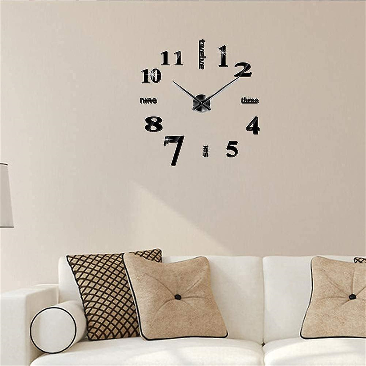 Wanduhr mit schwarzen Zahlen und Zeigern, an einer beigen Wand über einem Sofa montiert.
