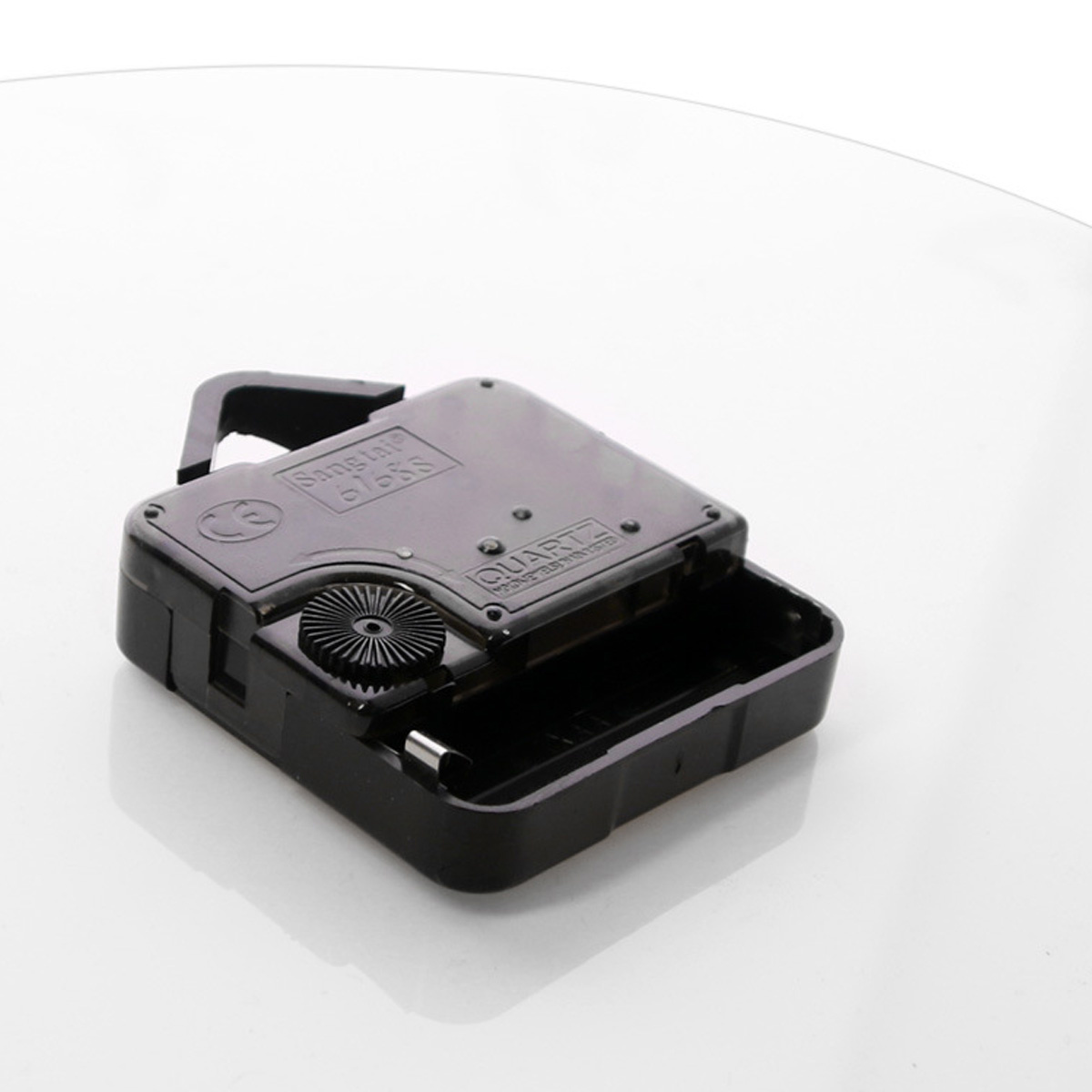 Ein schwarzer Uhrwerkmechanismus mit Batteriefach liegt auf einer weißen Oberfläche.