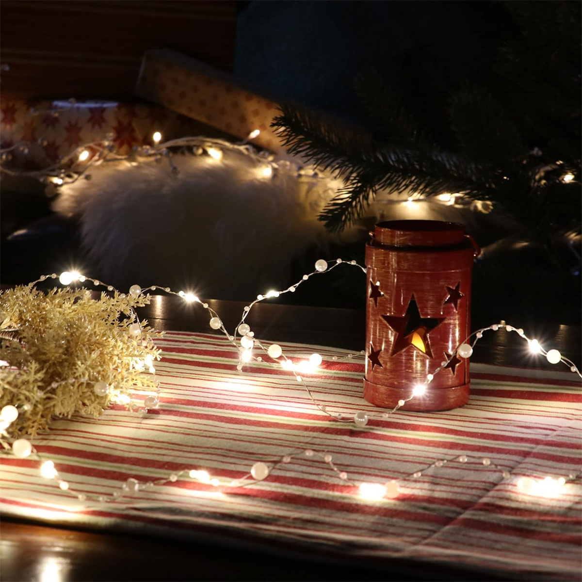 Weihnachtsbeleuchtung auf einem Tisch, roter Kerzenhalter im Hintergrund.