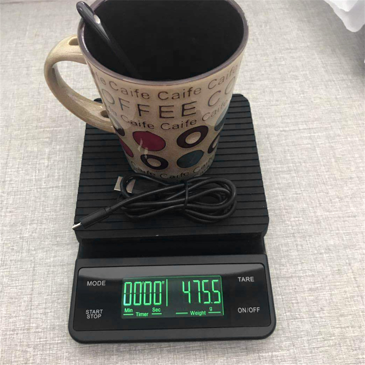 Schwarze digitale Kaffeewaage mit Tasse und Löffel oben drauf.