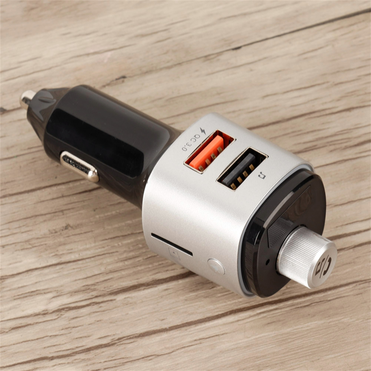 Schwarzes und silbernes Autoladegerät mit USB-Anschlüssen. Orangefarbene und schwarze Anschlüsse sichtbar. Holzuntergrund.