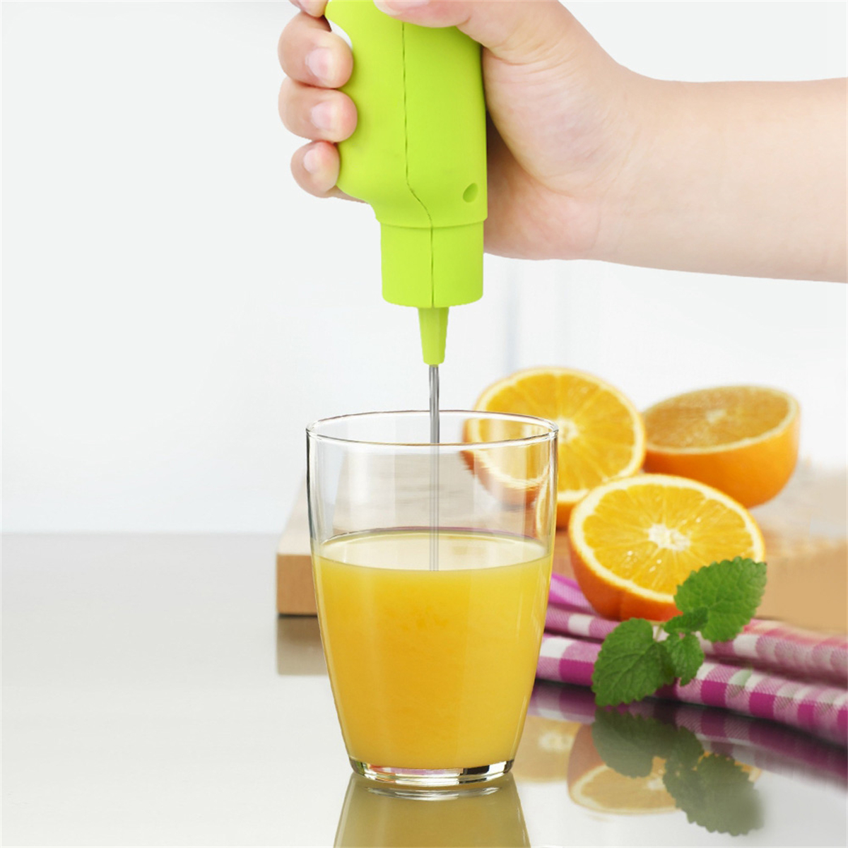 Eine Hand, die Orangensaft in einem klaren Glas mit einem elektrischen Mixer mixt, Orangen daneben.