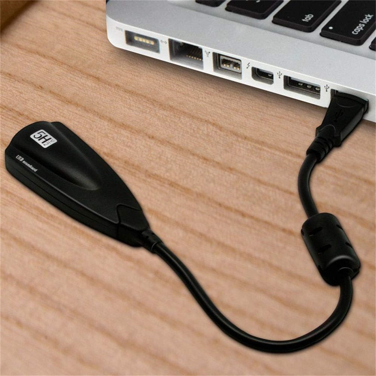 Schwarze USB-Soundkarte, die mit einem Laptop verbunden ist. Der USB-Stecker ist eingesteckt.