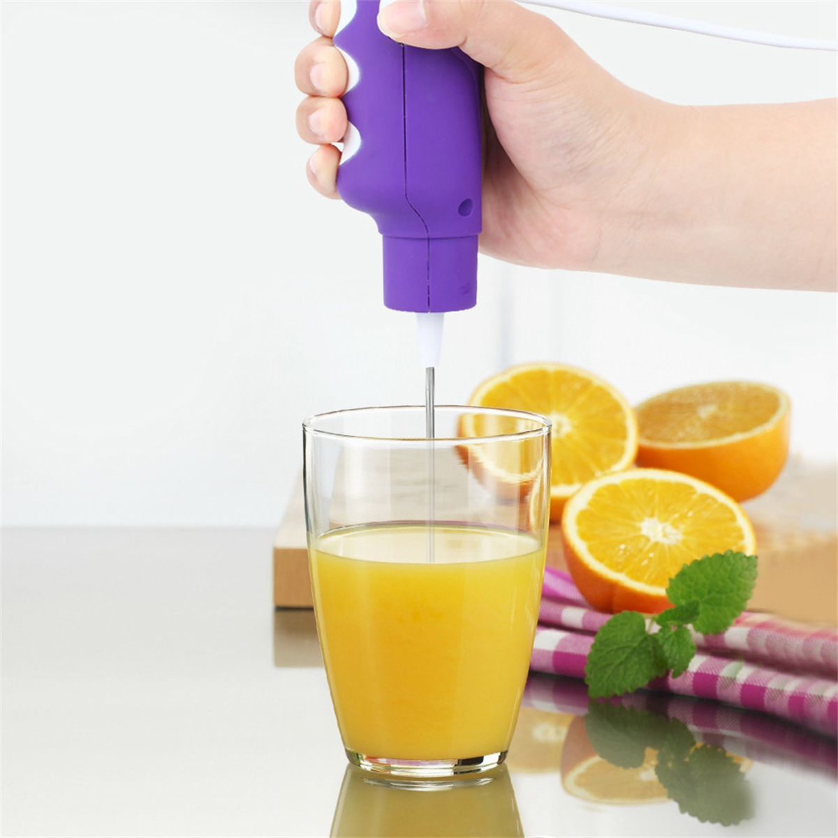 Orangensaft wird mit einem Handmixer zubereitet. Aufgeschnittene Orangen, Minze und ein Glas sind sichtbar.