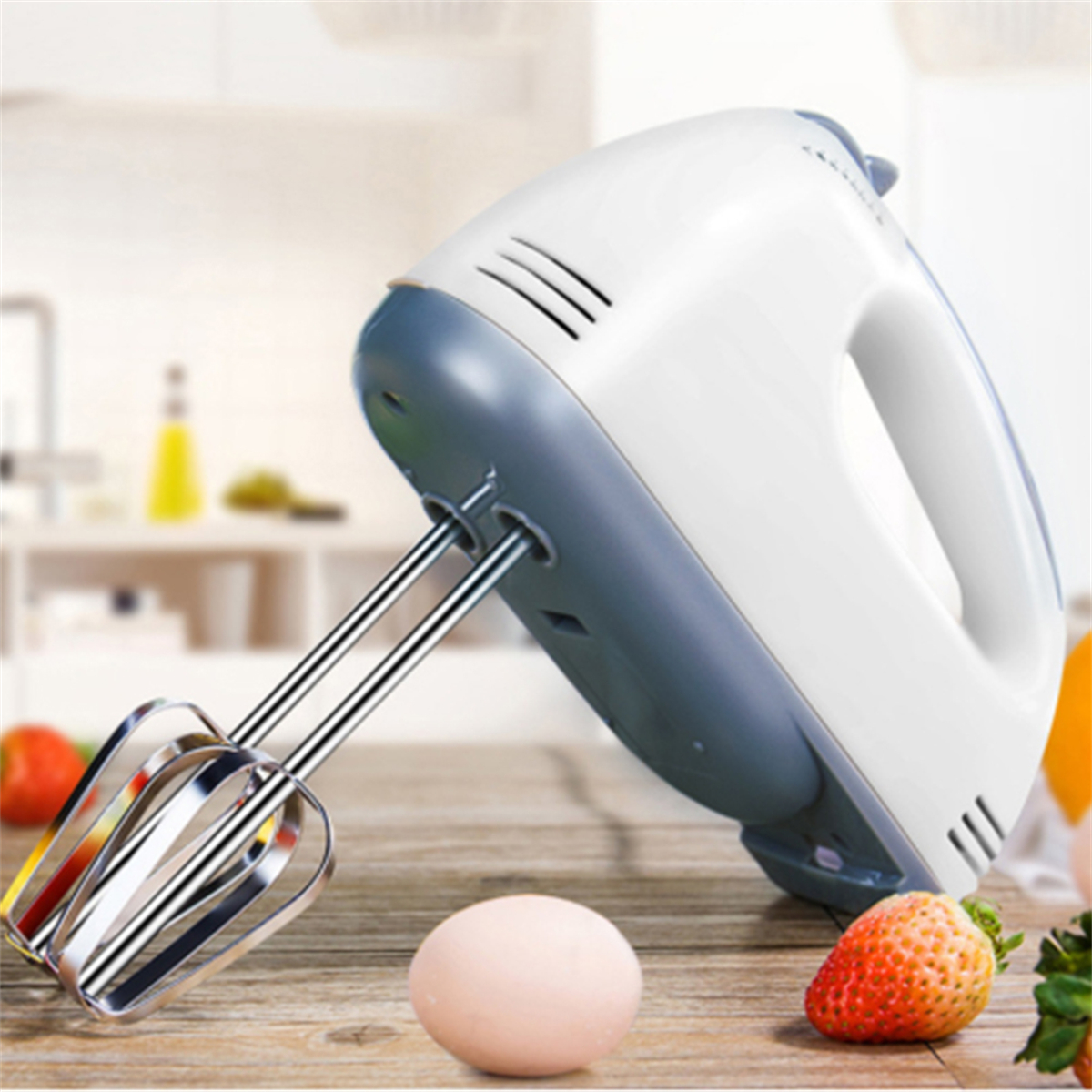 Weißer und grauer Handmixer mit Rührbesen, auf einer Holzoberfläche mit Ei und Erdbeere.