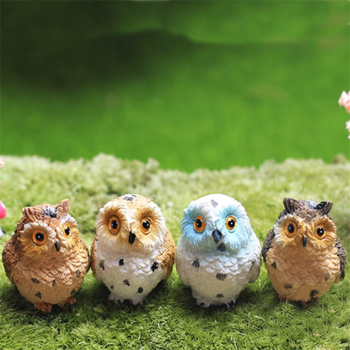 Vier Eulenfiguren in einer Reihe auf grünem Moos. Die Eulen haben unterschiedliche Farben und Merkmale.
