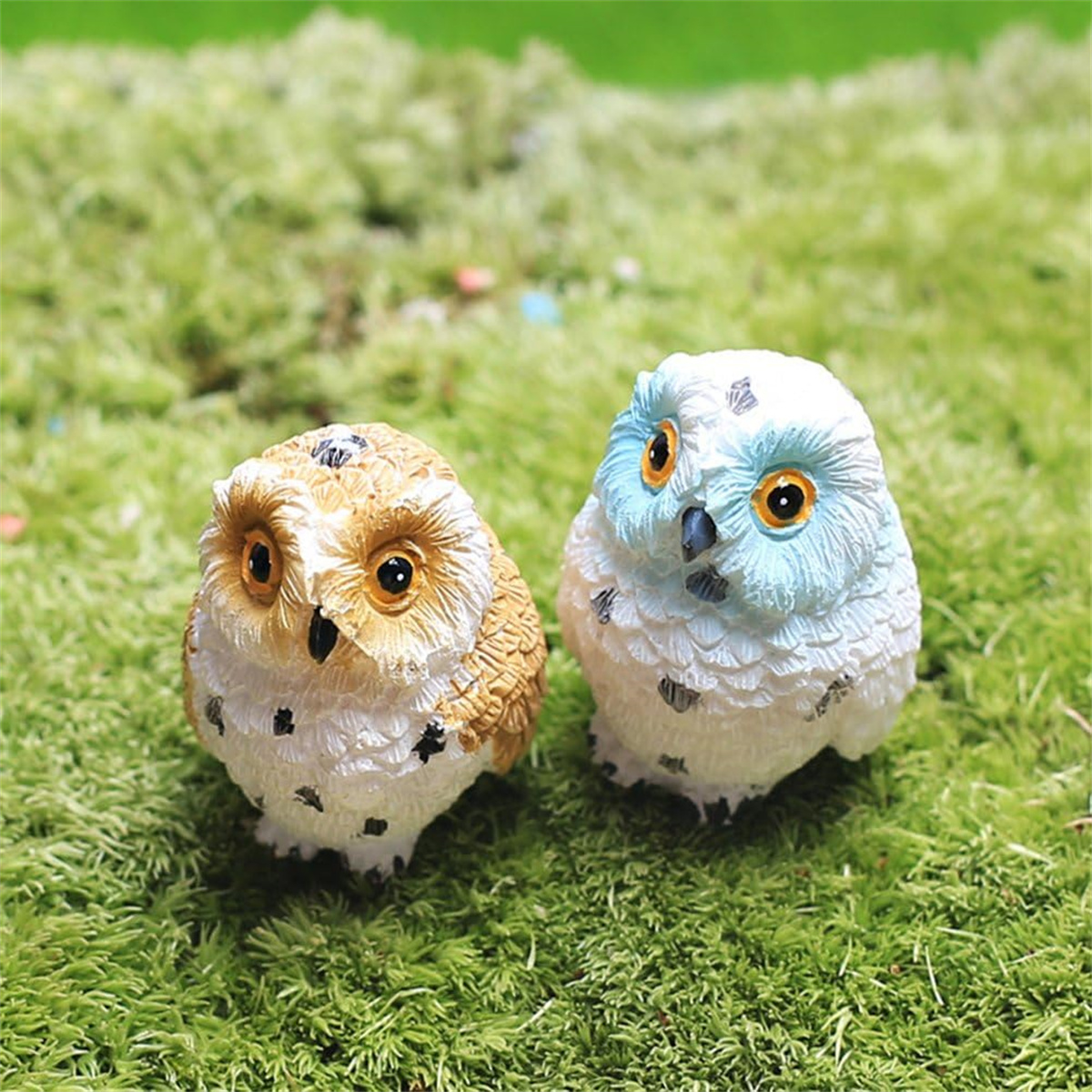 Zwei Eulenfiguren auf einer grasbewachsenen Oberfläche. Eine ist braun, die andere blau.