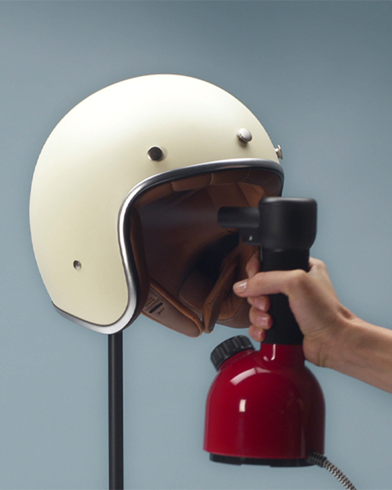 Cremefarbener Helm wird von einem rot-schwarzen Dampfer bedampft. Blauer Hintergrund.