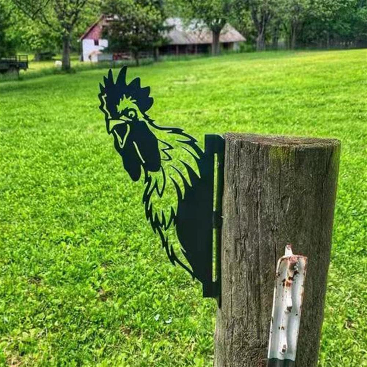 Eine schwarze Metall-Hahnen-Silhouette auf einem Holzpfosten in einem grasbewachsenen Feld, mit grünem Hintergrund.