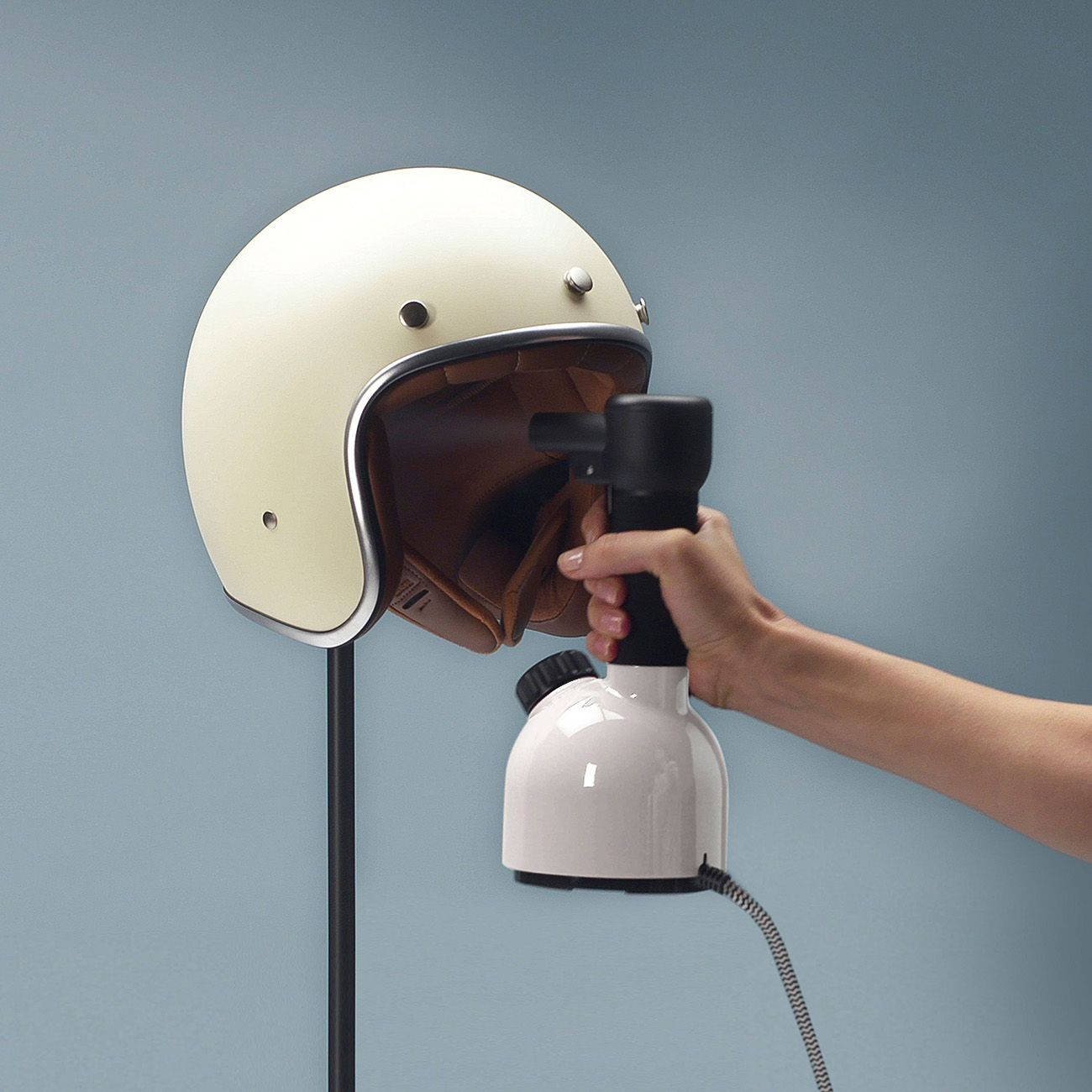 Cremefarbener Helm, der mit einem Reinigungsgerät besprüht wird, auf Blau.