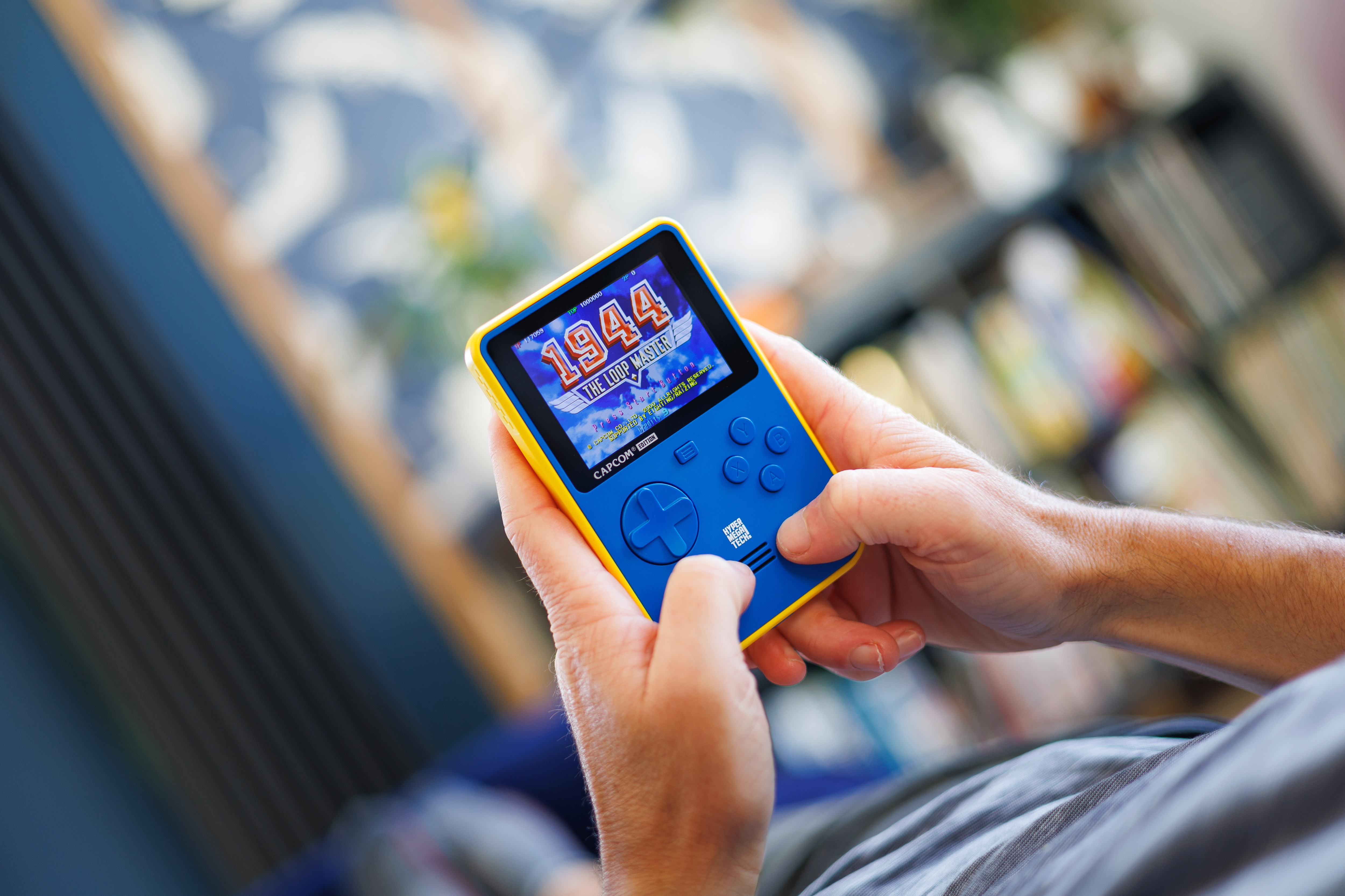 Osoba trzyma żółto-niebieską konsolę przenośną. Ekran pokazuje grę z tekstem.