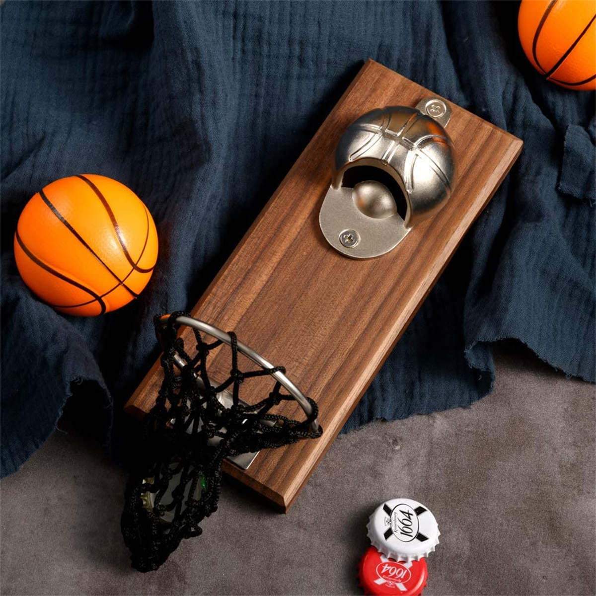 Ein Holzflaschenöffner in Form eines Basketballkorbs, mit zwei Kronkorken in der Nähe und einem orangefarbenen Ball.