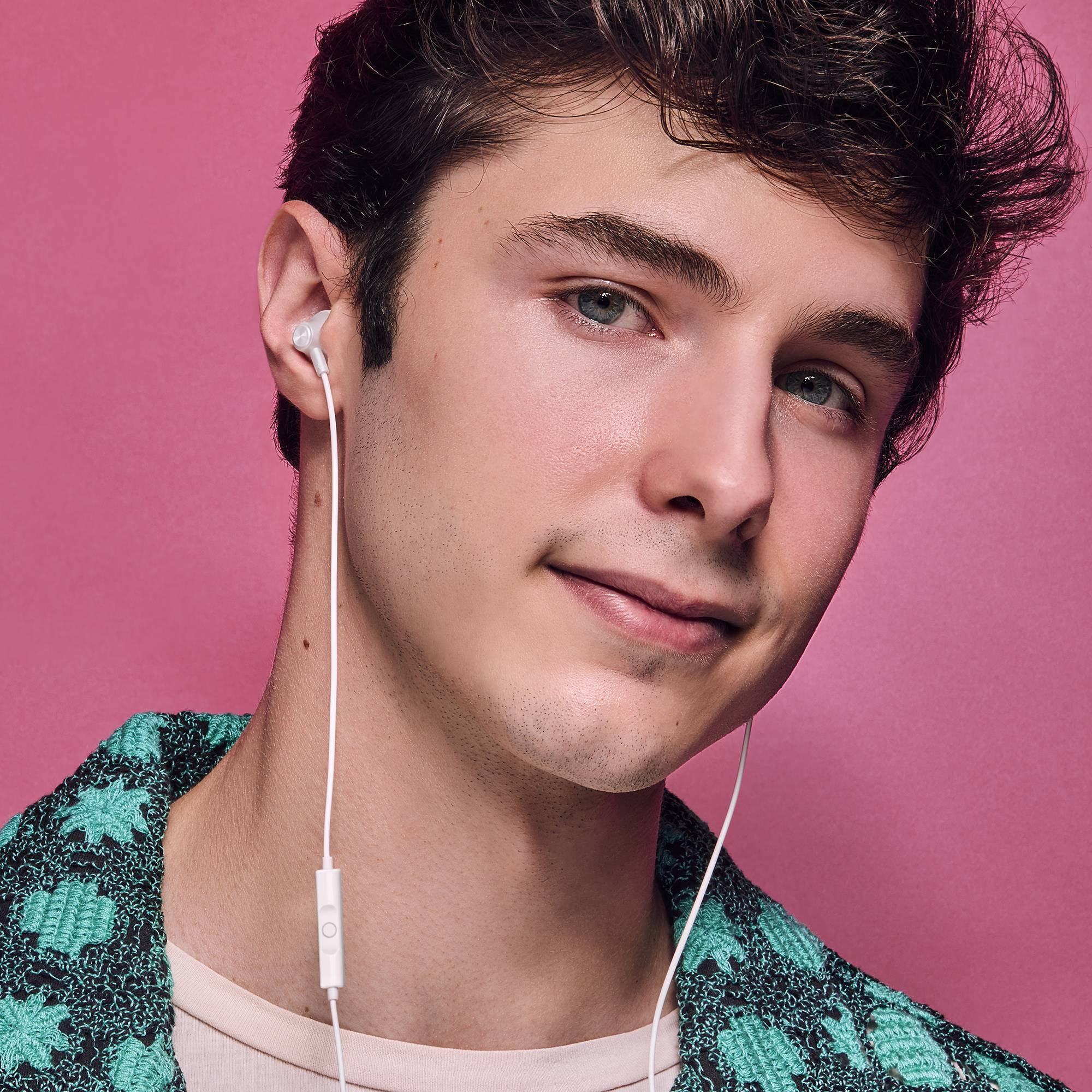 Jonge man met witte oortjes, roze achtergrond. Draagt een patroonshirt.