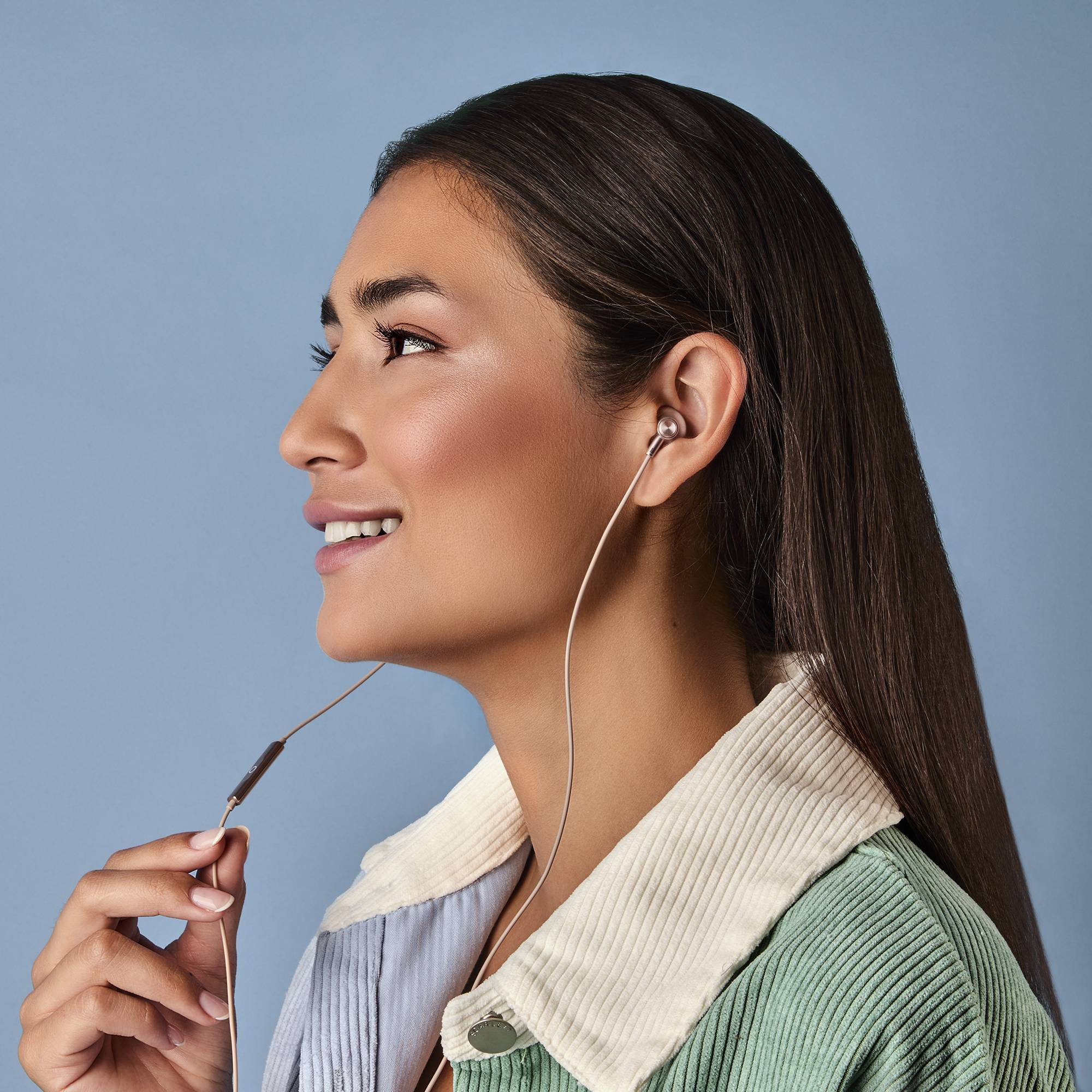 Donna con auricolari, sorridente, guarda a sinistra. Indossa giacca verde e camicia a righe.