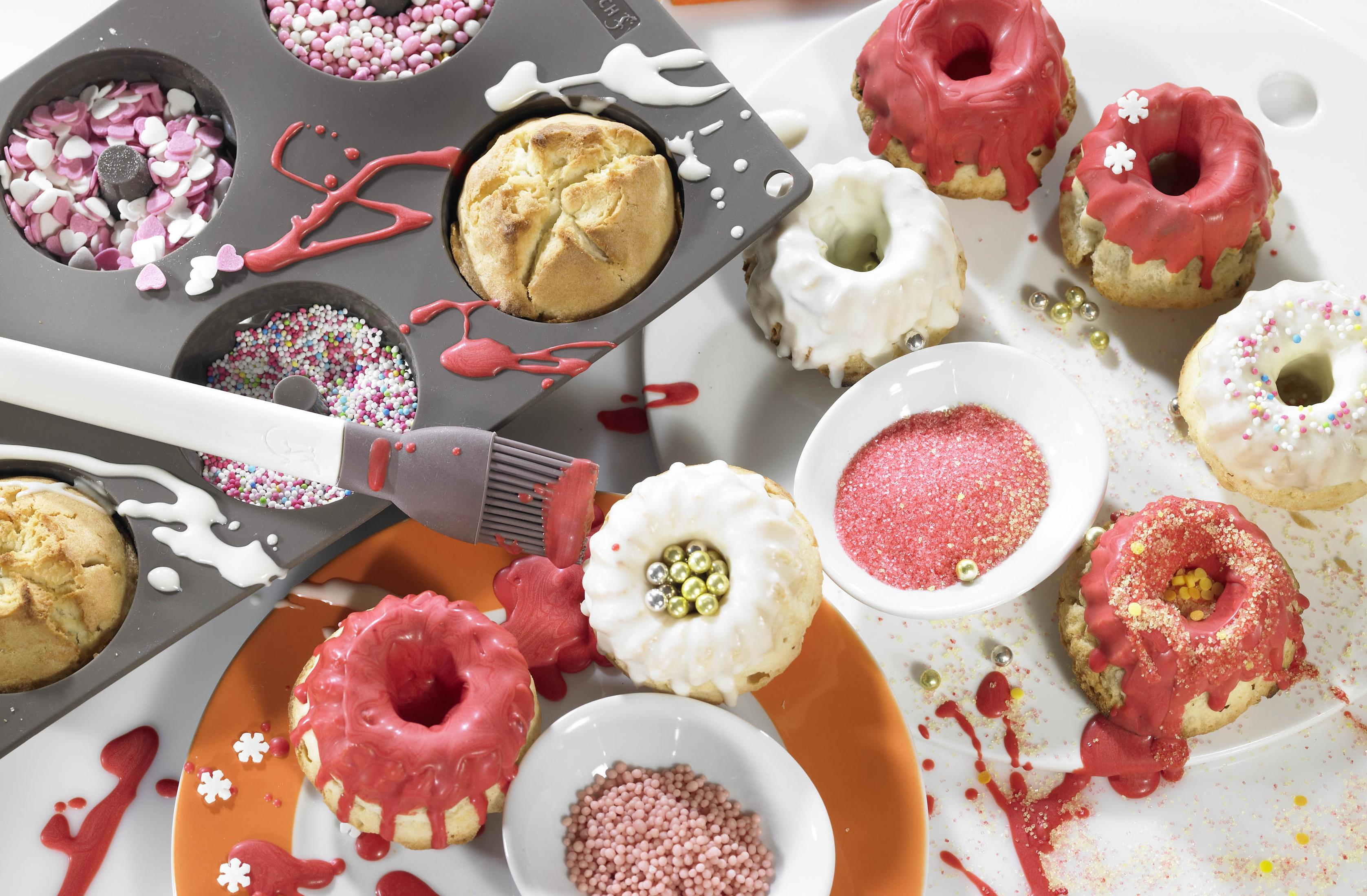 Donuts mit roter und weißer Glasur, Streuseln und einem Pinsel auf weißem Untergrund.