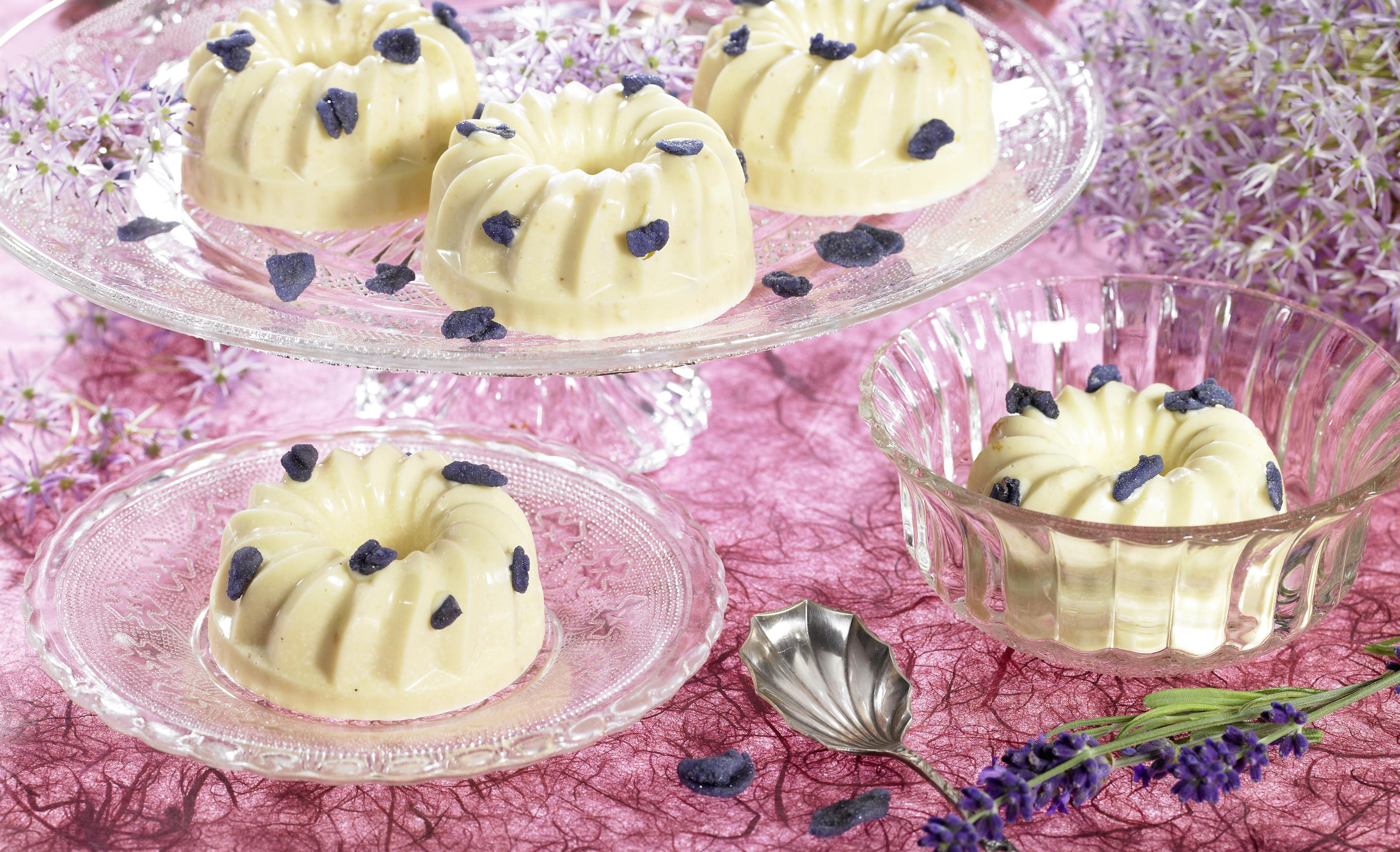 Desserts in Ringform mit blauen Streuseln werden auf Glastellern und -schalen auf einem rosa Tisch präsentiert.