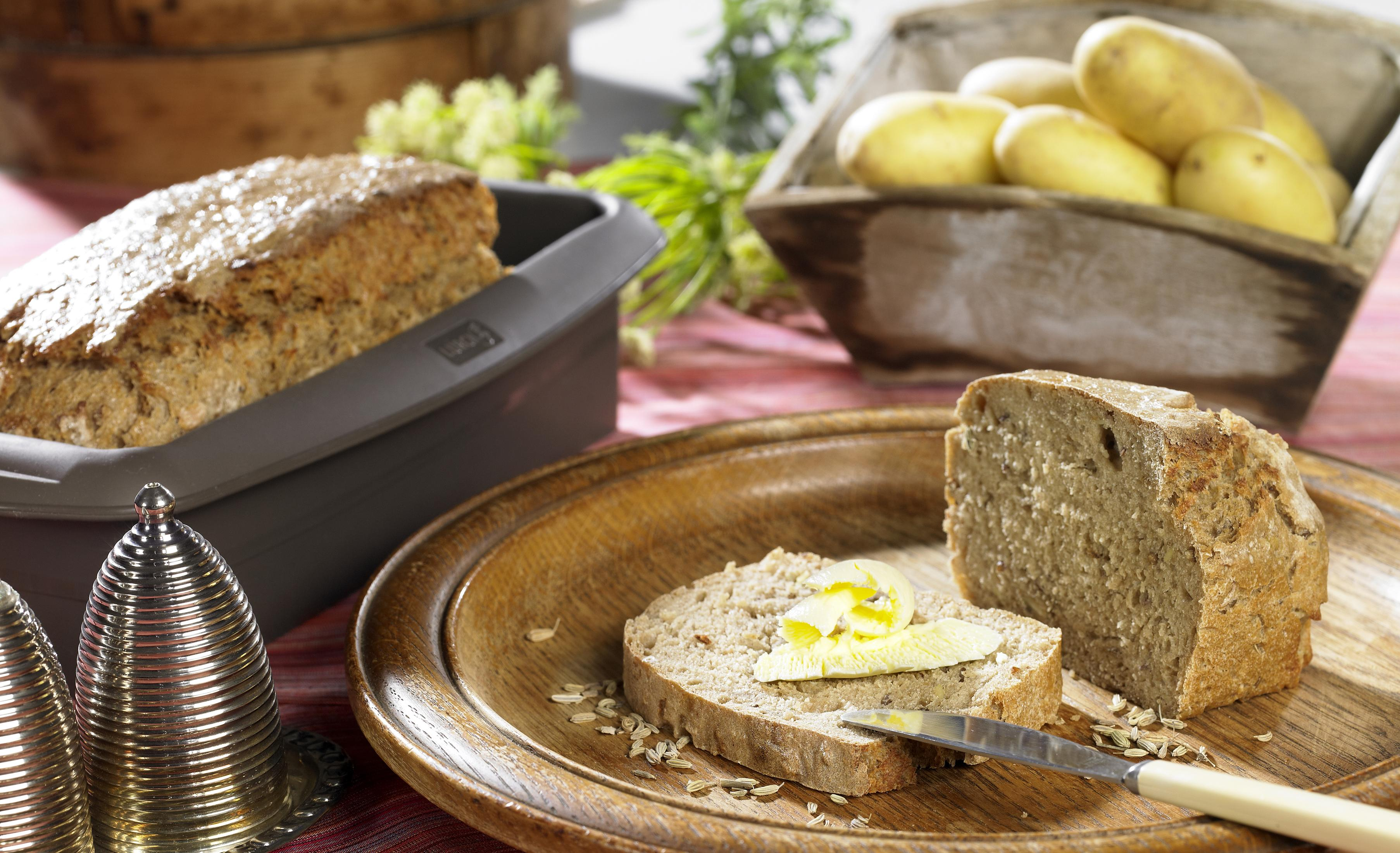 Kawałek chleba z masłem na drewnianym talerzu. Chleb w pojemniku i ziemniaki.