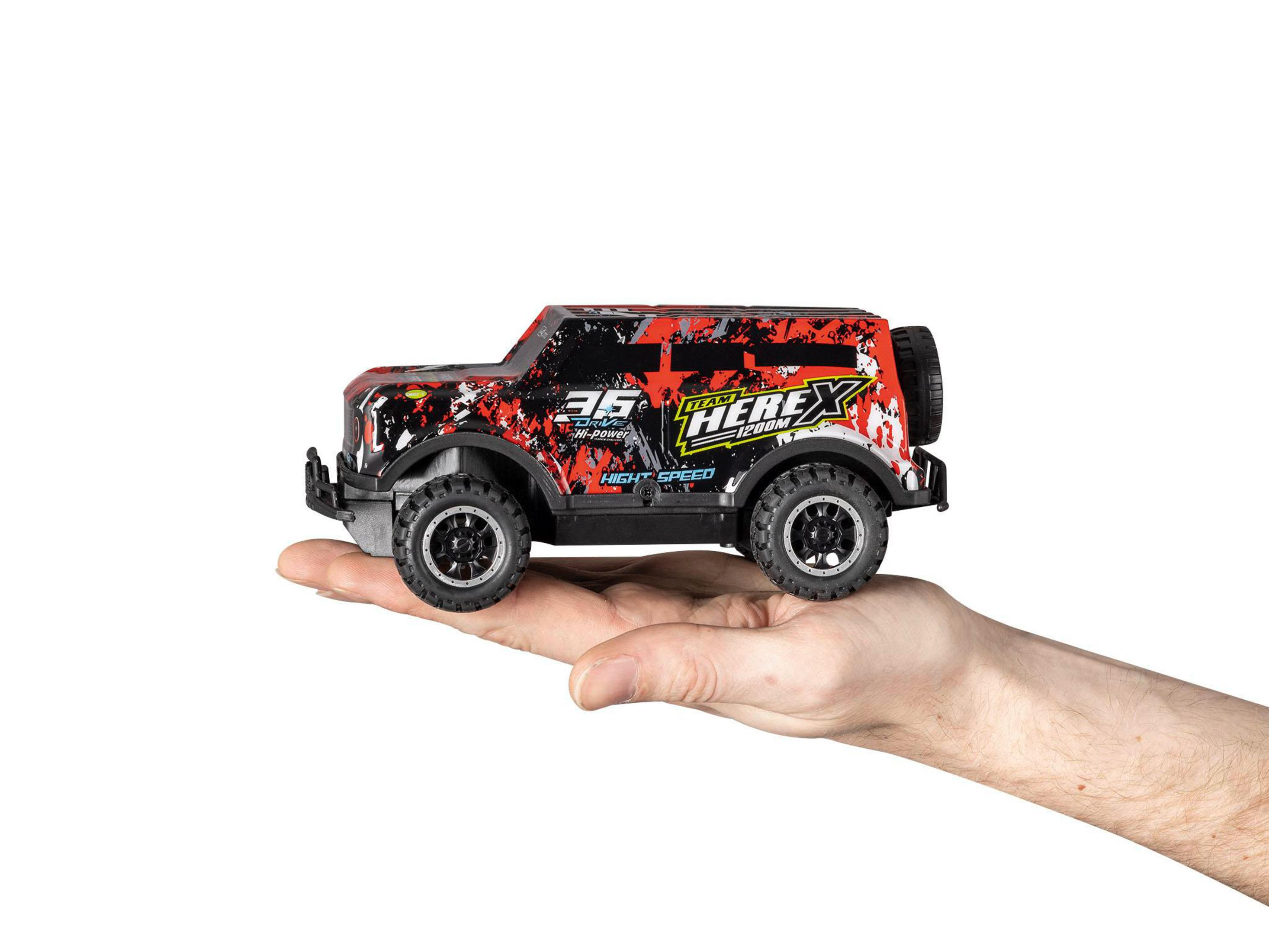 Coche de juguete rojo y negro pequeño en una mano, fondo blanco.