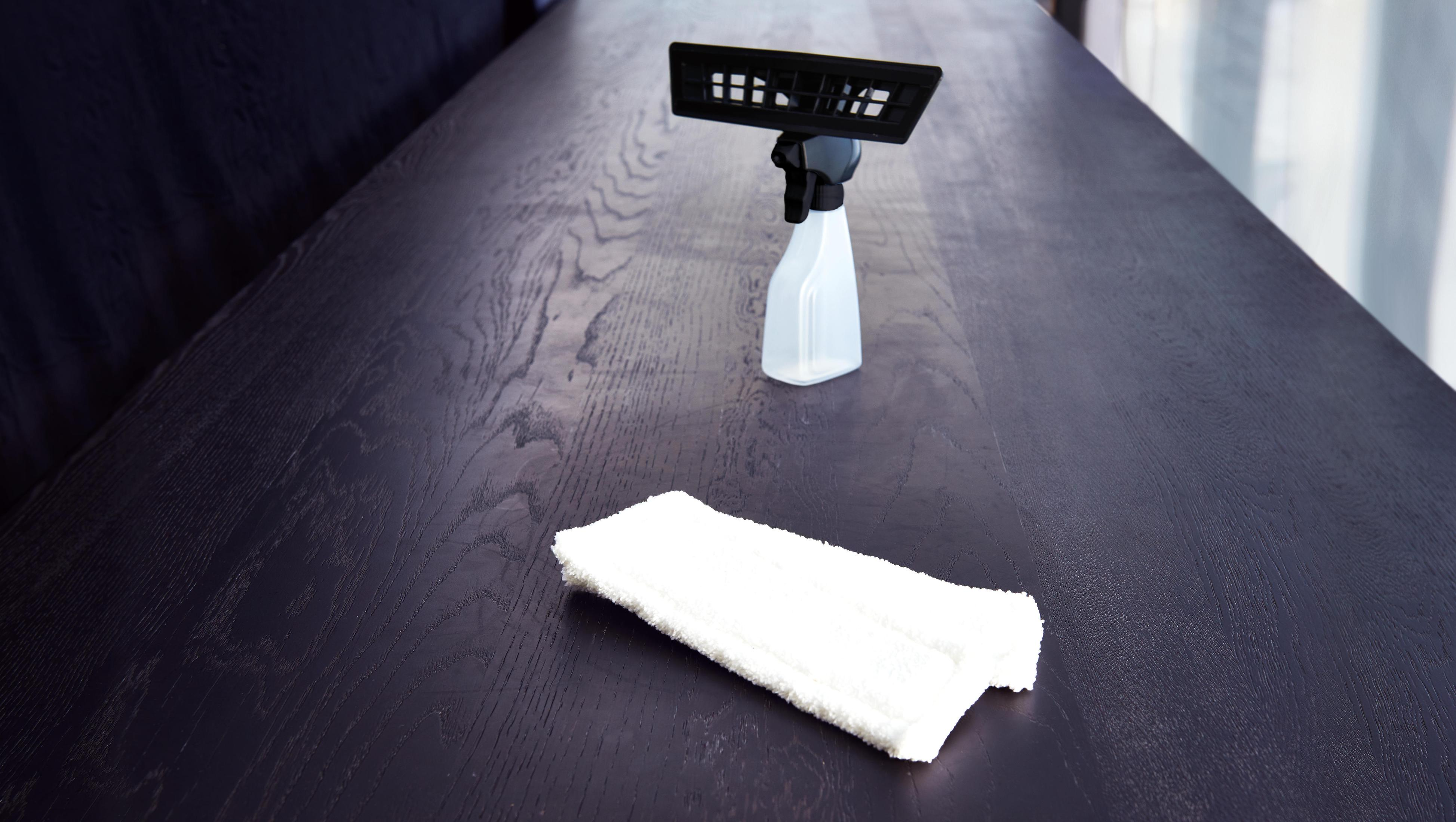 Un flacone spray per la pulizia e un panno bianco su un tavolo di legno scuro.