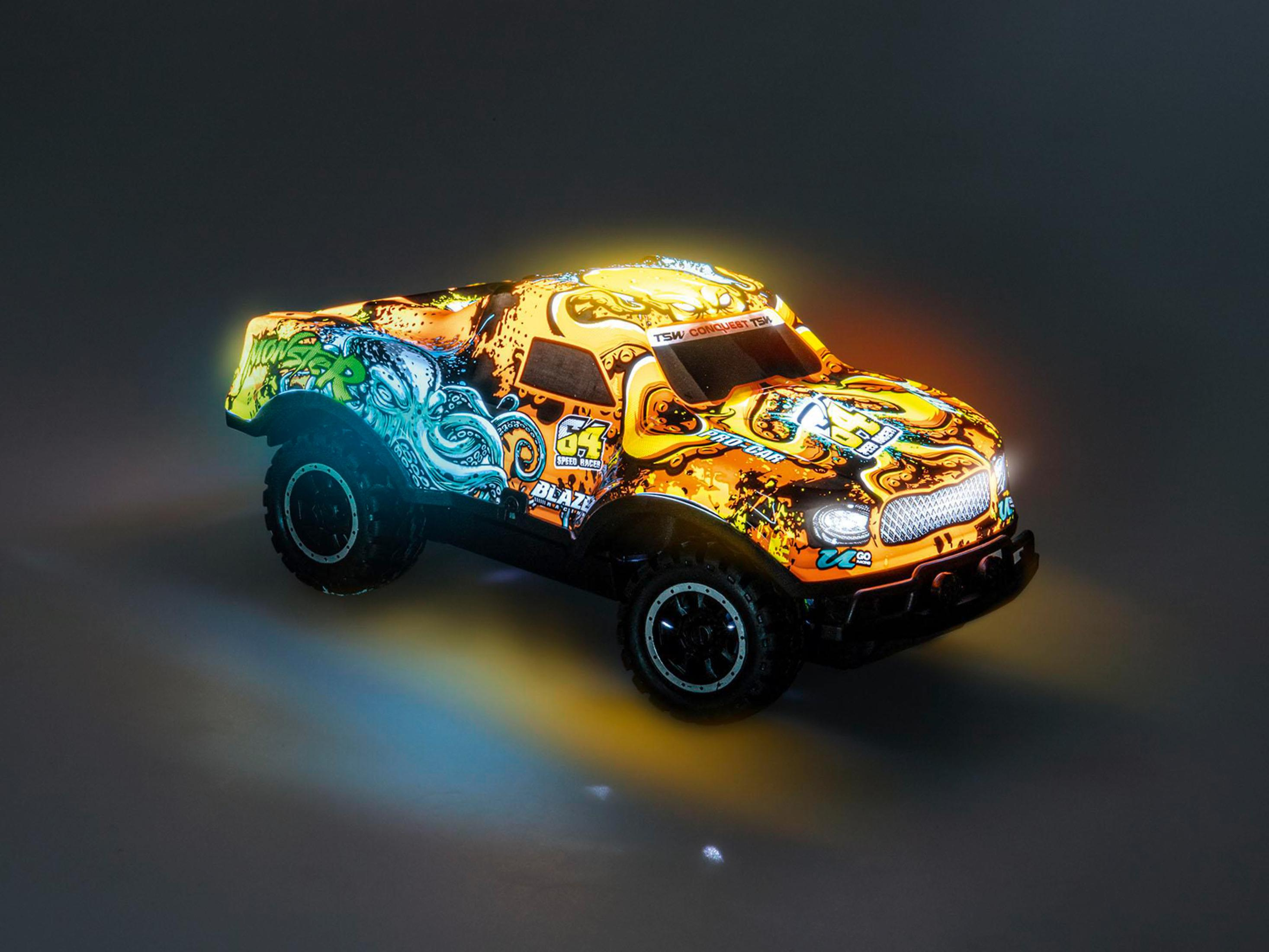 Ein Spielzeug-Monstertruck mit farbenfrohem Design steht auf einer reflektierenden Oberfläche. Die Lichter sind an.