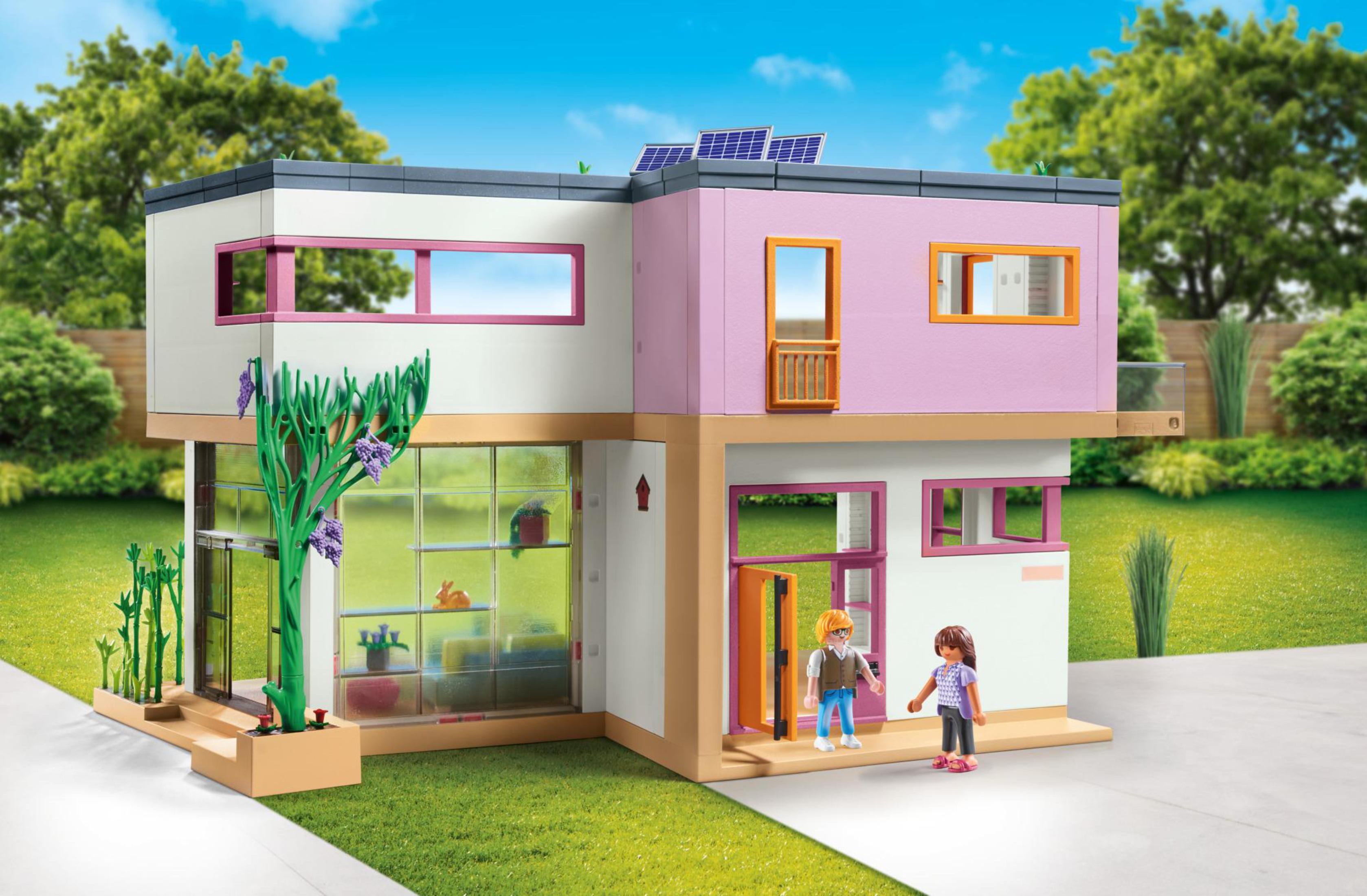 Ein modernes Spielzeughaus mit Sonnenkollektoren und zwei Figuren davor.