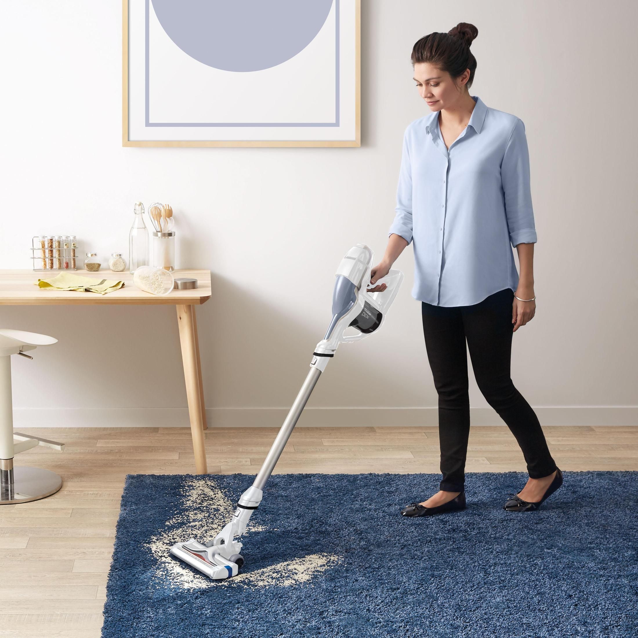 Frau, die einen blauen Teppich saugt, mit Staubsauger und Holztisch im Hintergrund.