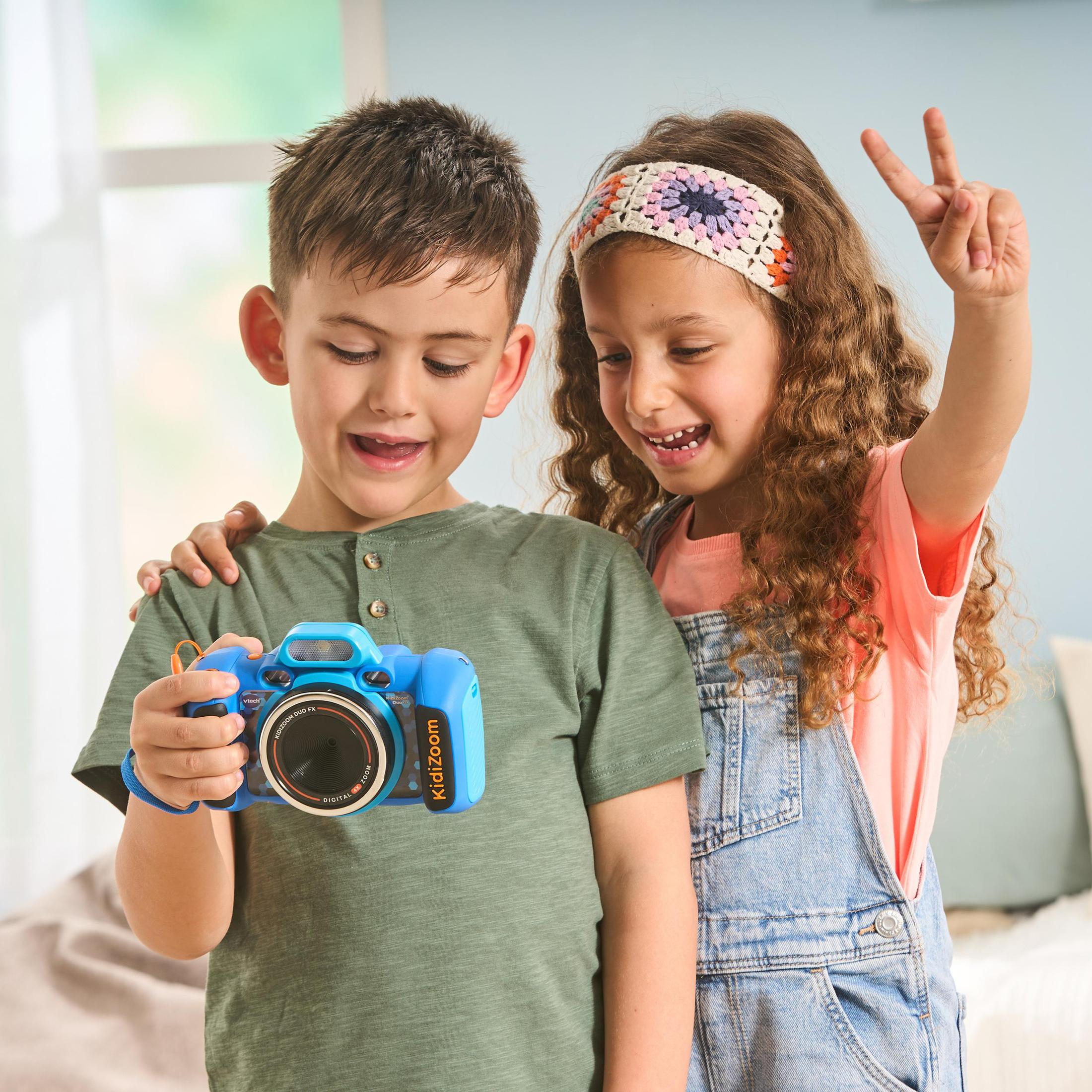 Zwei Kinder betrachten eine blaue Spielzeugkamera. Ein Kind zeigt zwei Finger.