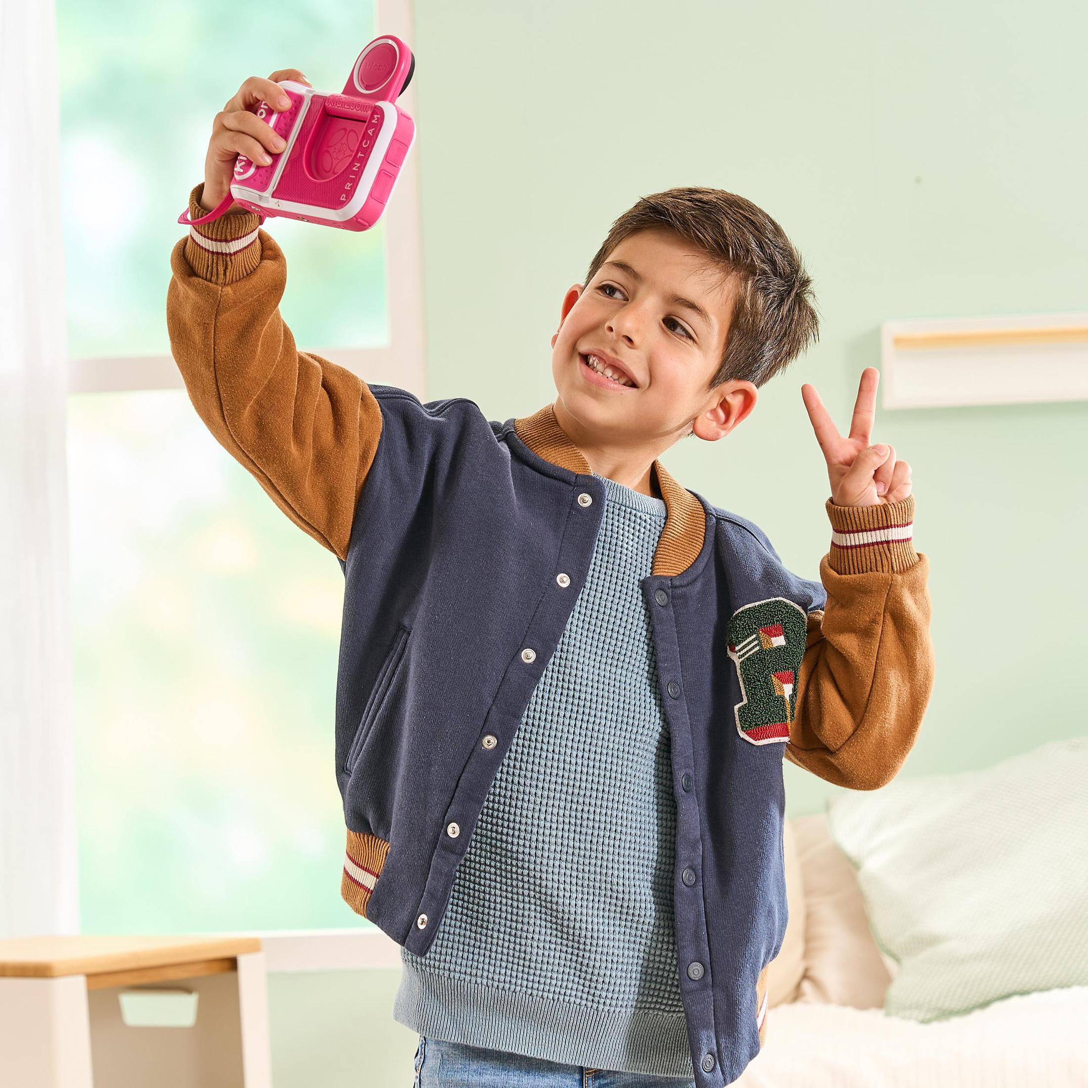 Junger Junge macht Selfie mit einer rosa Spielzeugkamera, lächelnd.