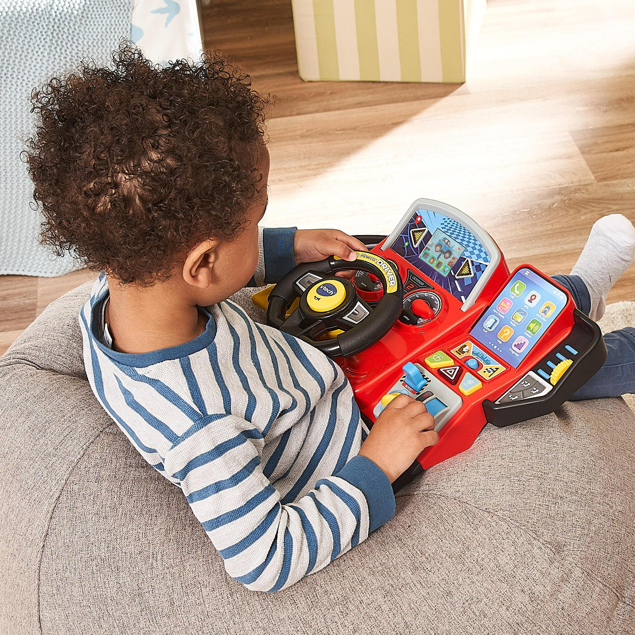Enfant jouant avec une voiture jouet rouge. L'enfant est de dos. Le fond est un pouf et un jouet.
