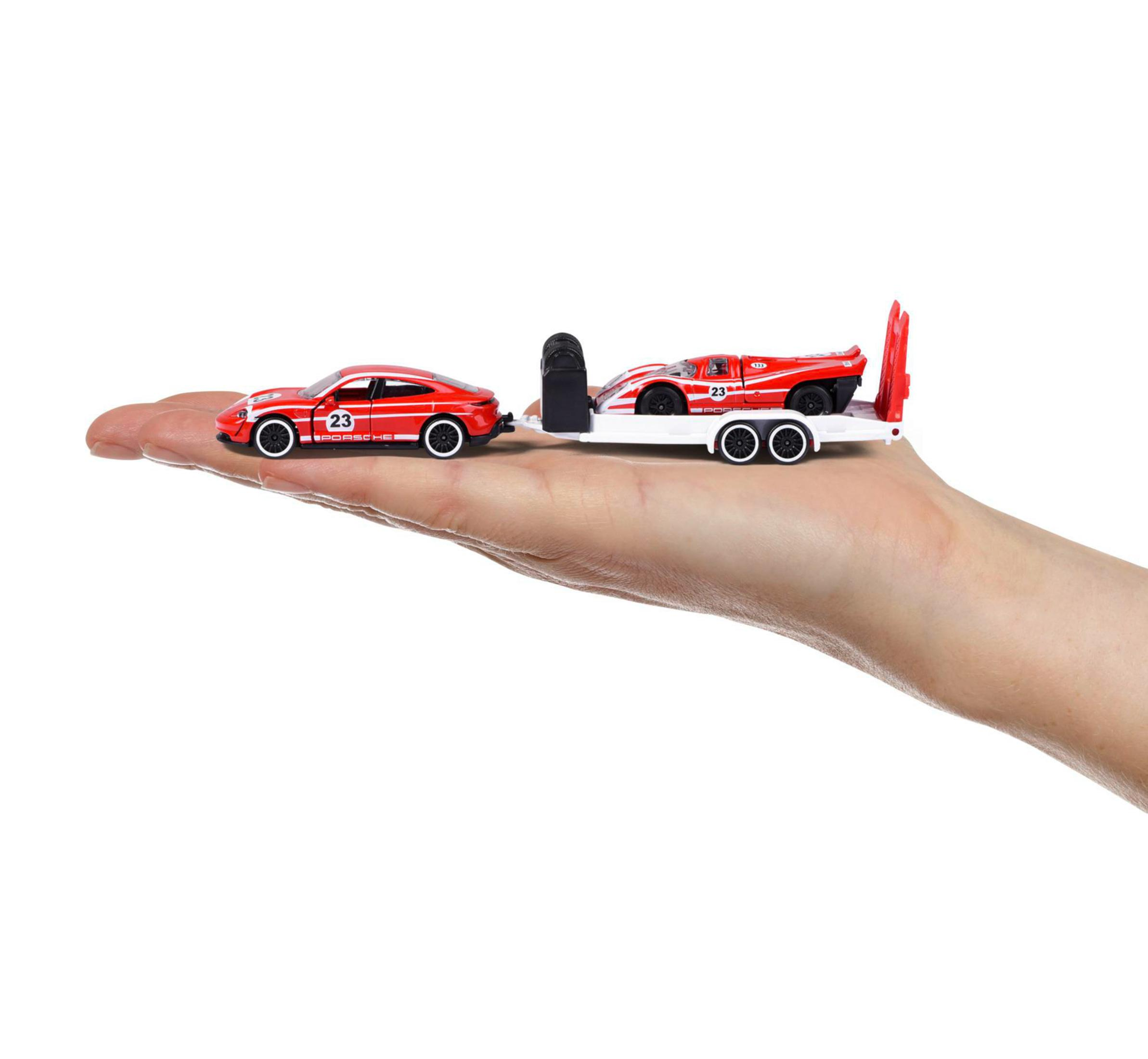 Hand, die Spielzeugautos hält, ein roter Sportwagen und ein rotes Rennauto auf einem Anhänger.