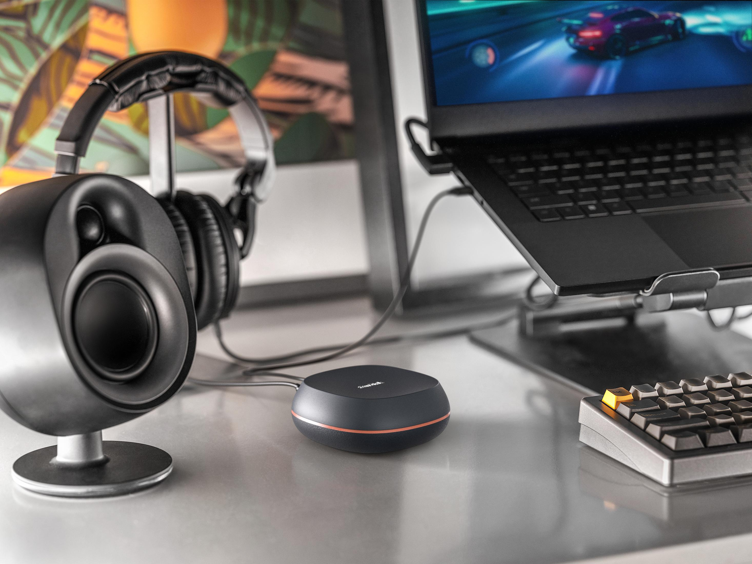 Konfiguracja biurka ze słuchawkami, głośnikami, laptopem i czarnym urządzeniem. Gra widoczna na ekranie laptopa.