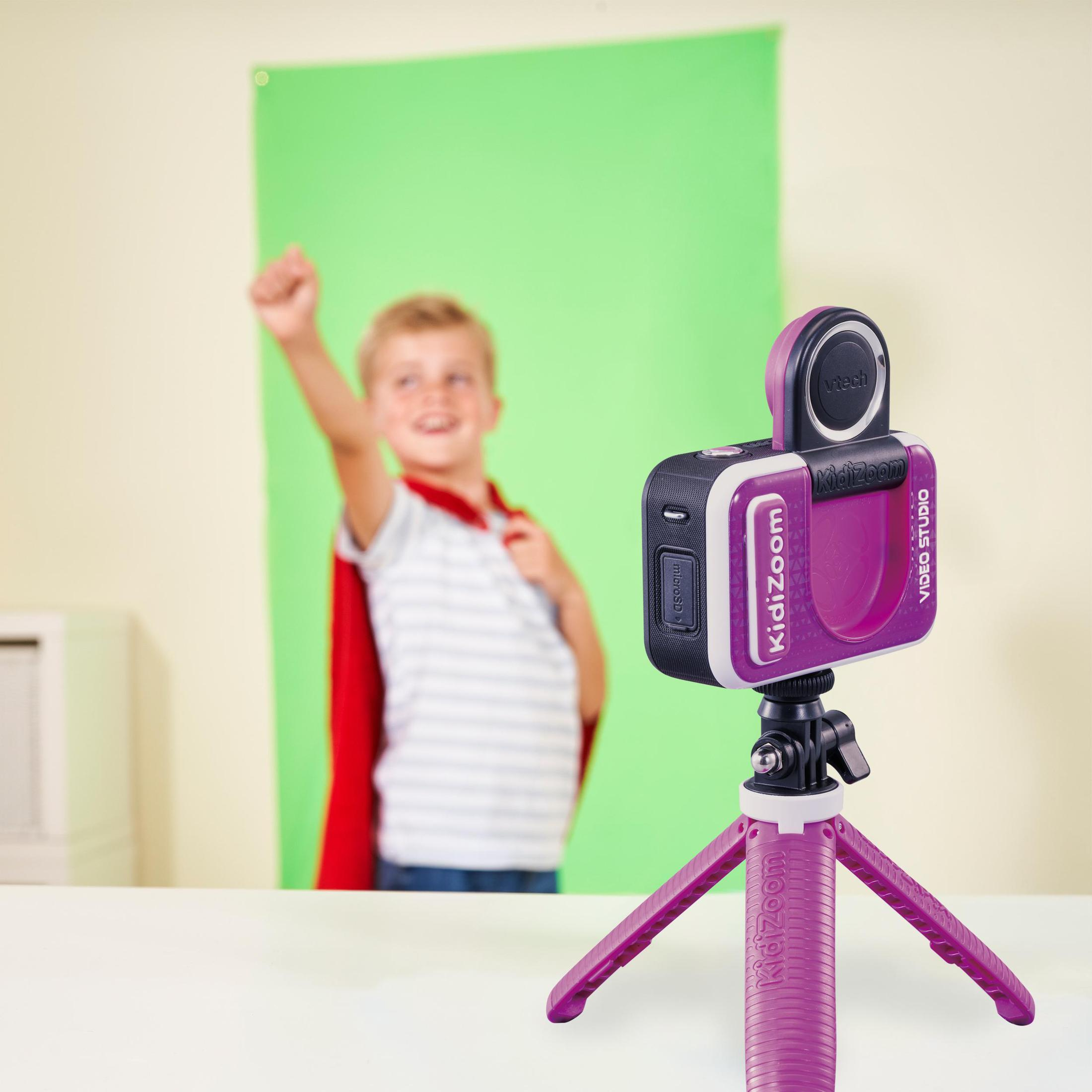 KidZoom-Videokamera auf einem Stativ, im Fokus. Ein Junge mit Umhang ist im Hintergrund unscharf, auf einer Green-Screen.