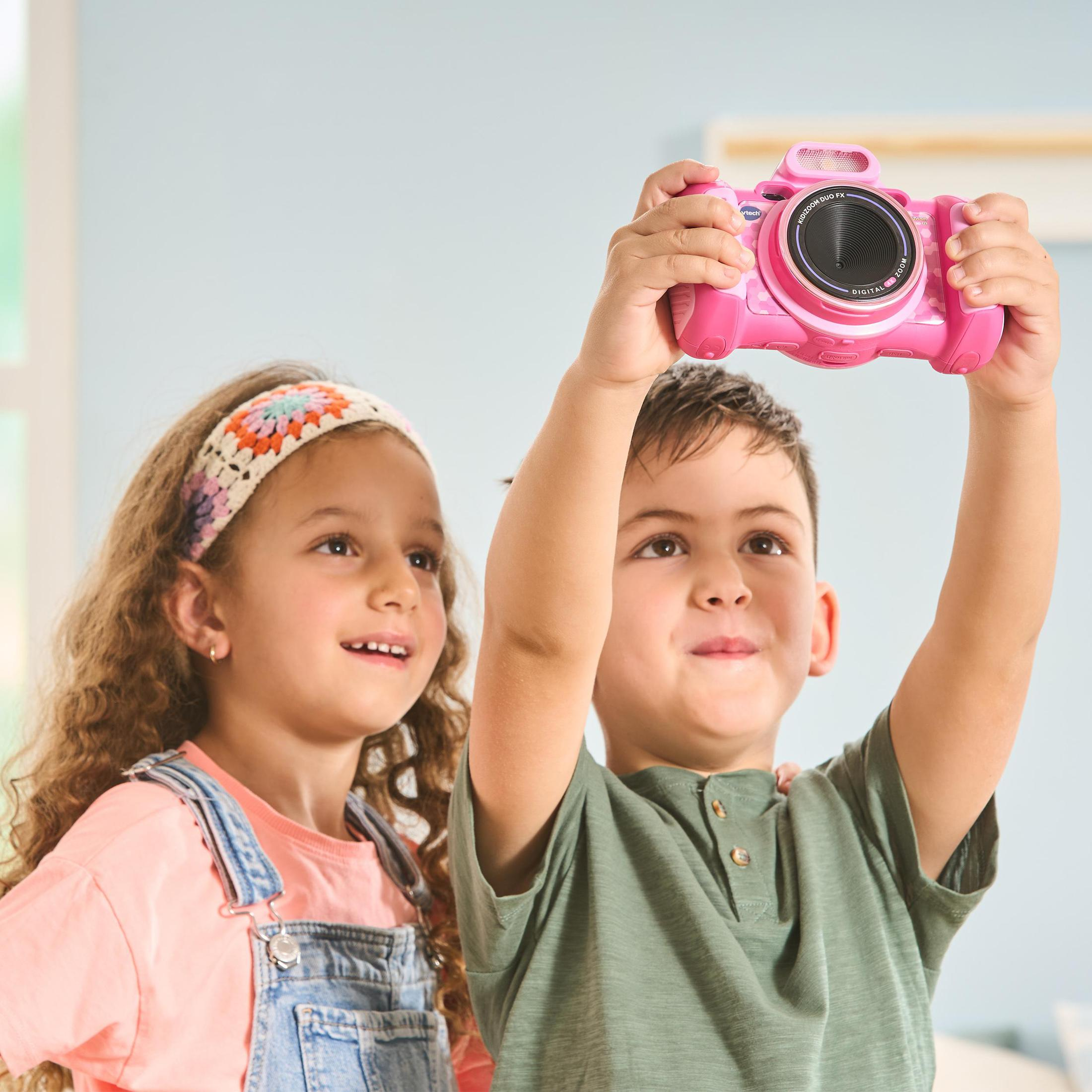 Zwei Kinder schauen nach oben, eines hält eine rosa Spielzeugkamera über dem Kopf.