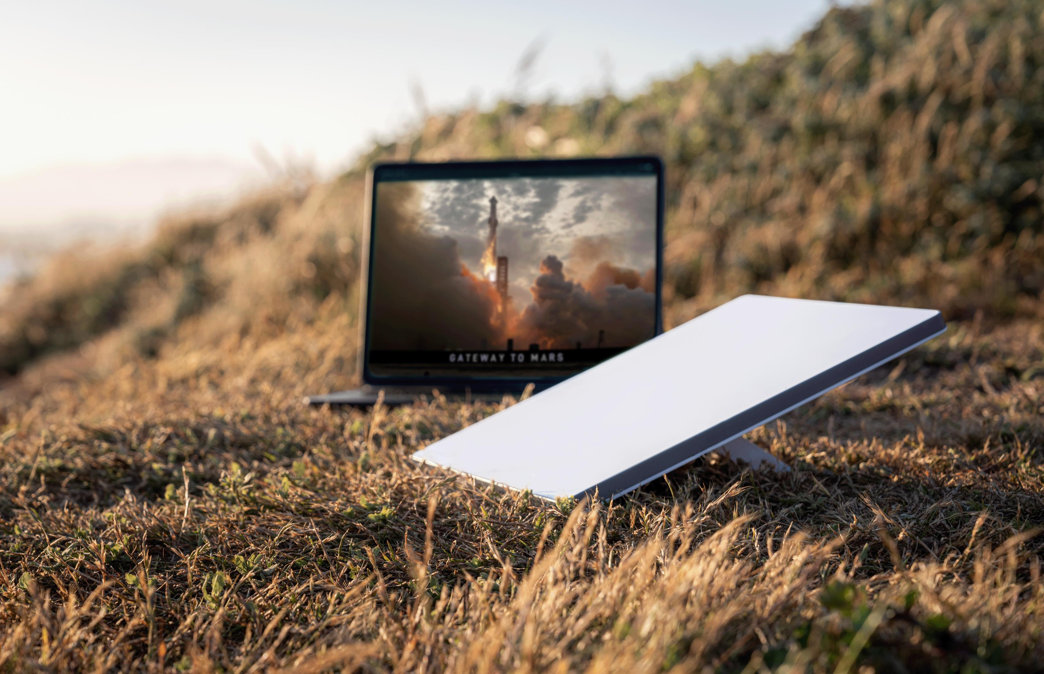 Laptop mit Weltraumstart, Satellitenschüssel auf Gras.