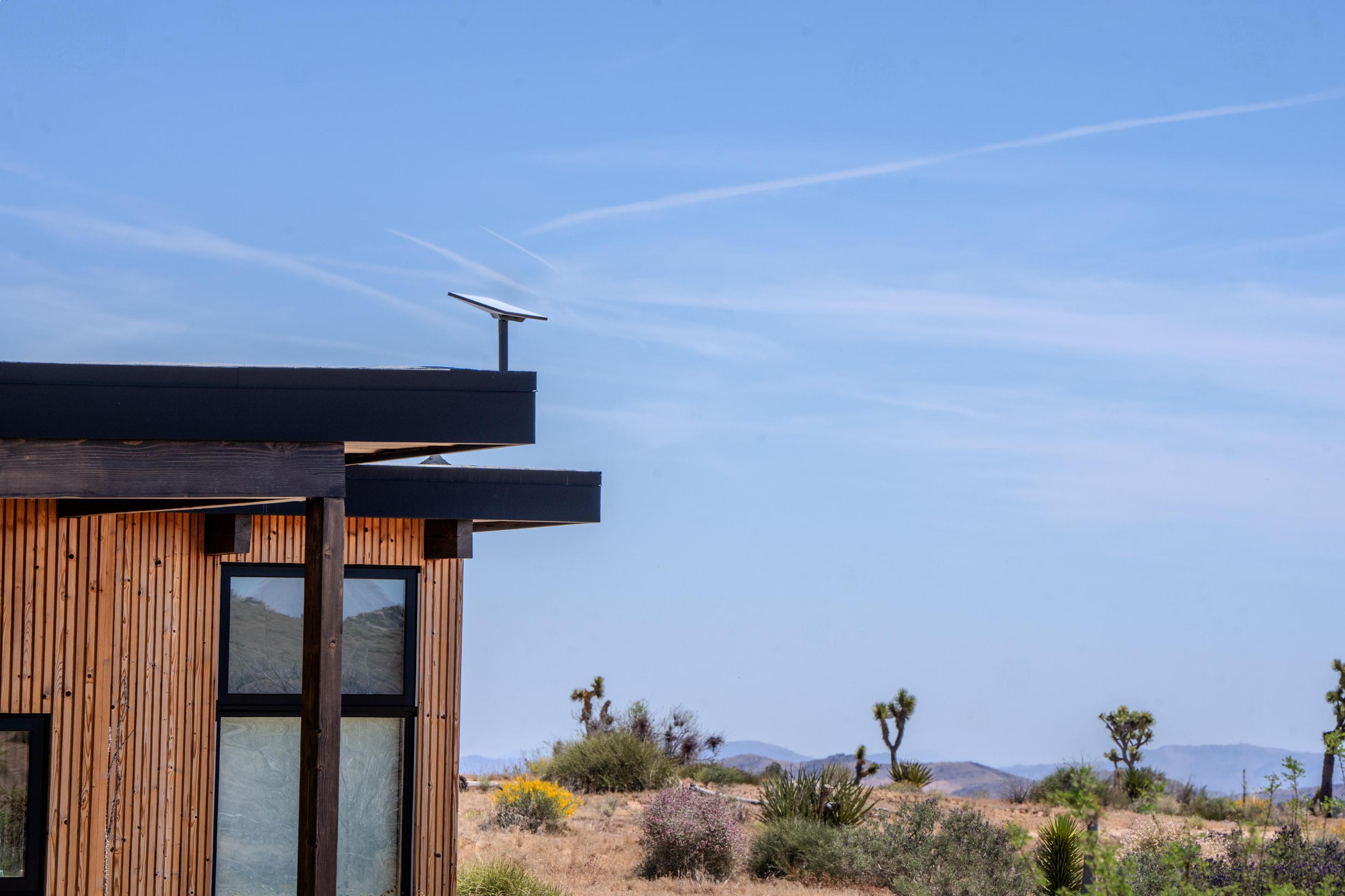 Modernes Haus mit Holzverkleidung. Solarpanel auf dem Dach. Blauer Himmel und Wüstenlandschaft.