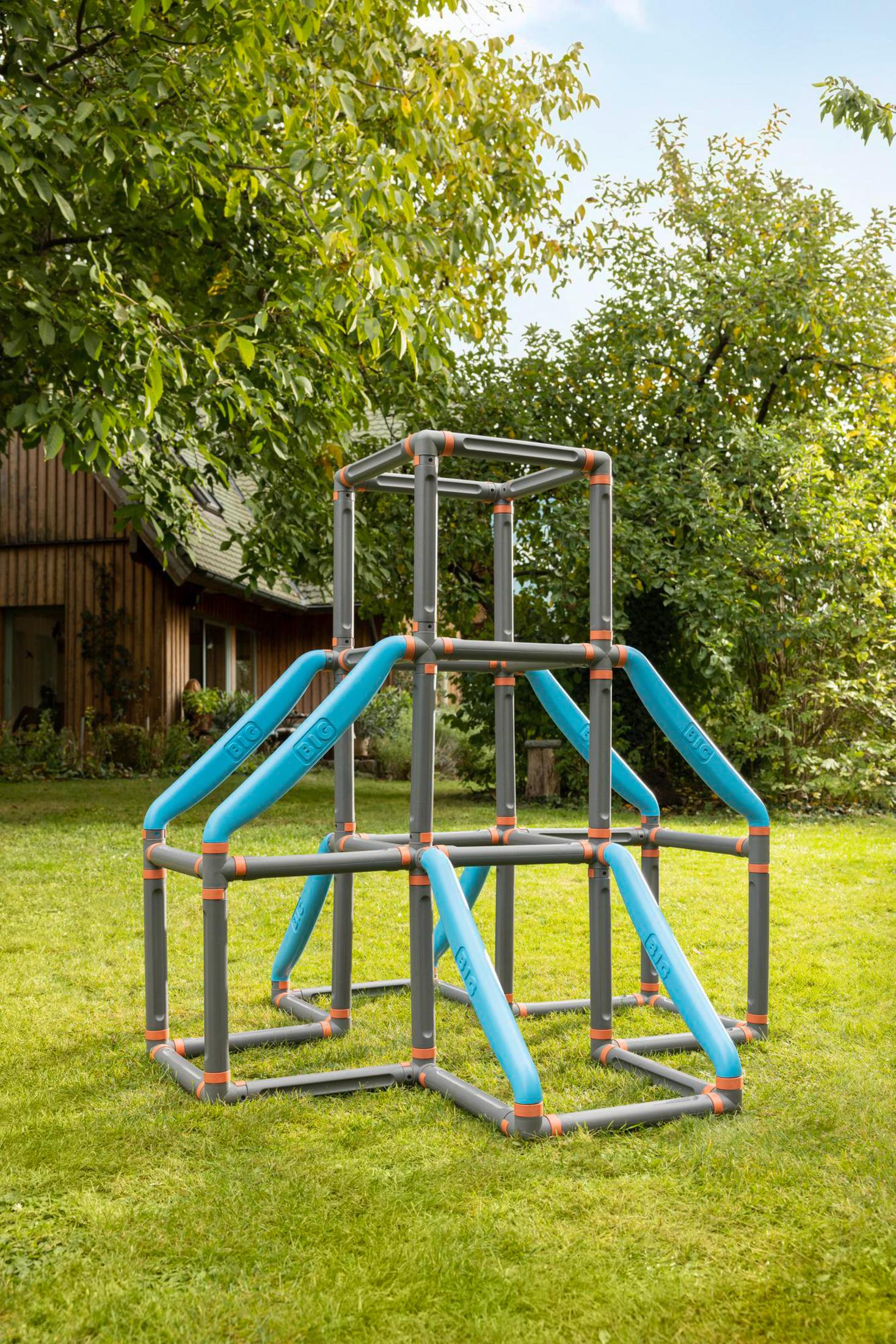 Spielgerüst im Freien mit blauen Stangen und grauen Stützen, in einem grasbewachsenen Garten.