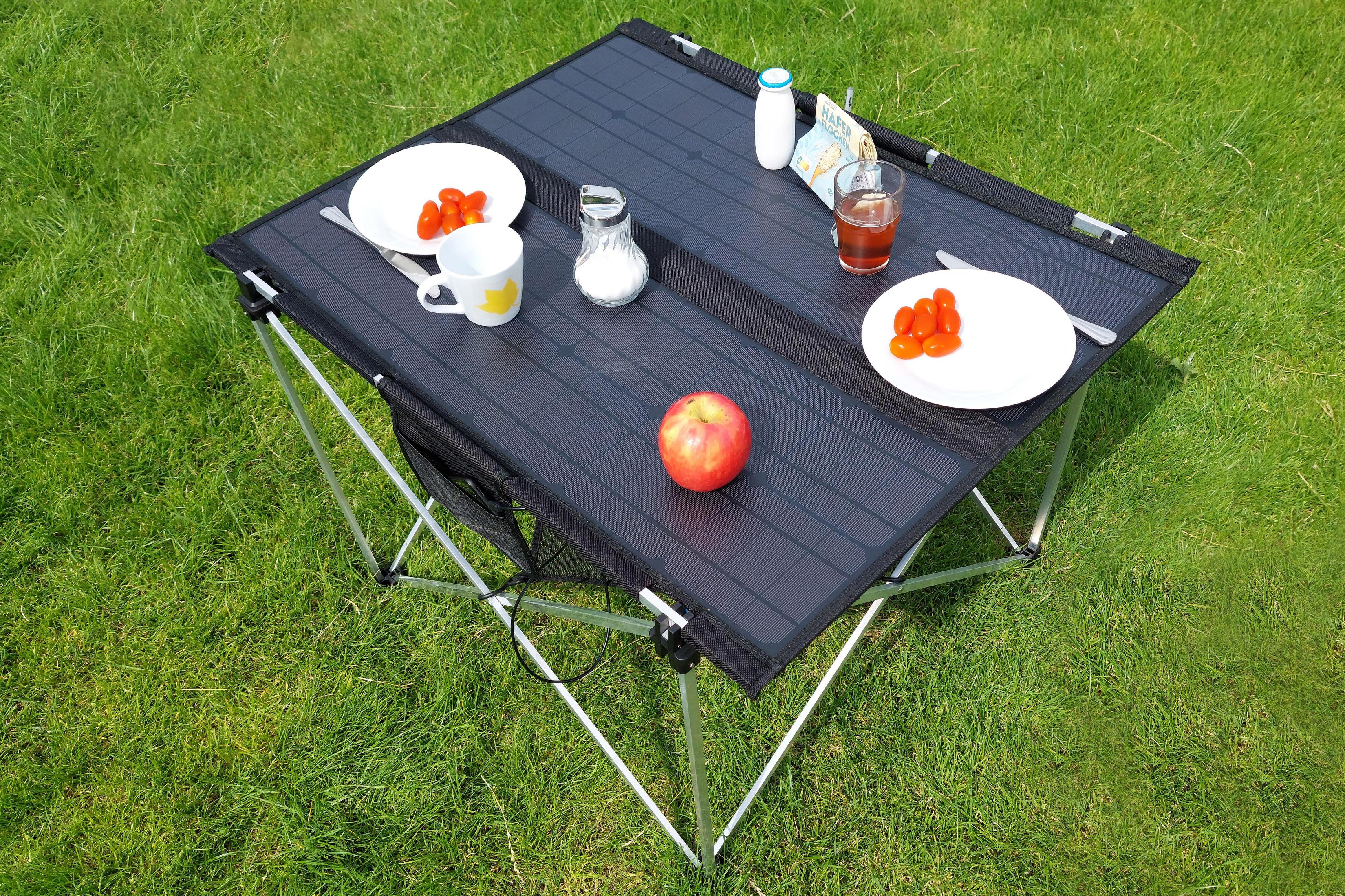 Un tavolo da picnic sull'erba con cibo e bevande. Il tavolo è nero con gambe argentate.