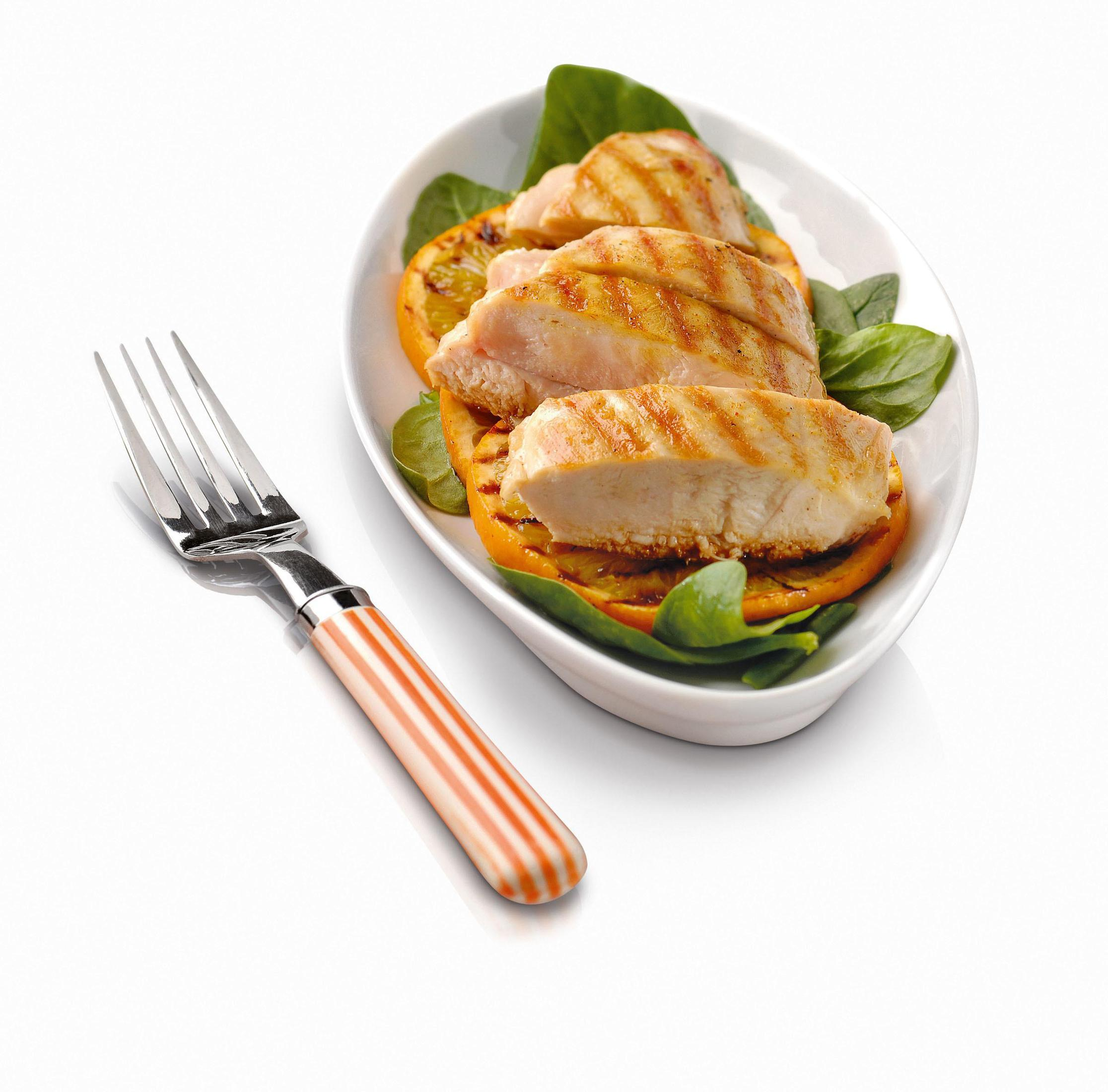 Gegrillte Hähnchenbrustscheiben auf einem Teller mit Spinat und Orangenscheiben, mit einer Gabel.