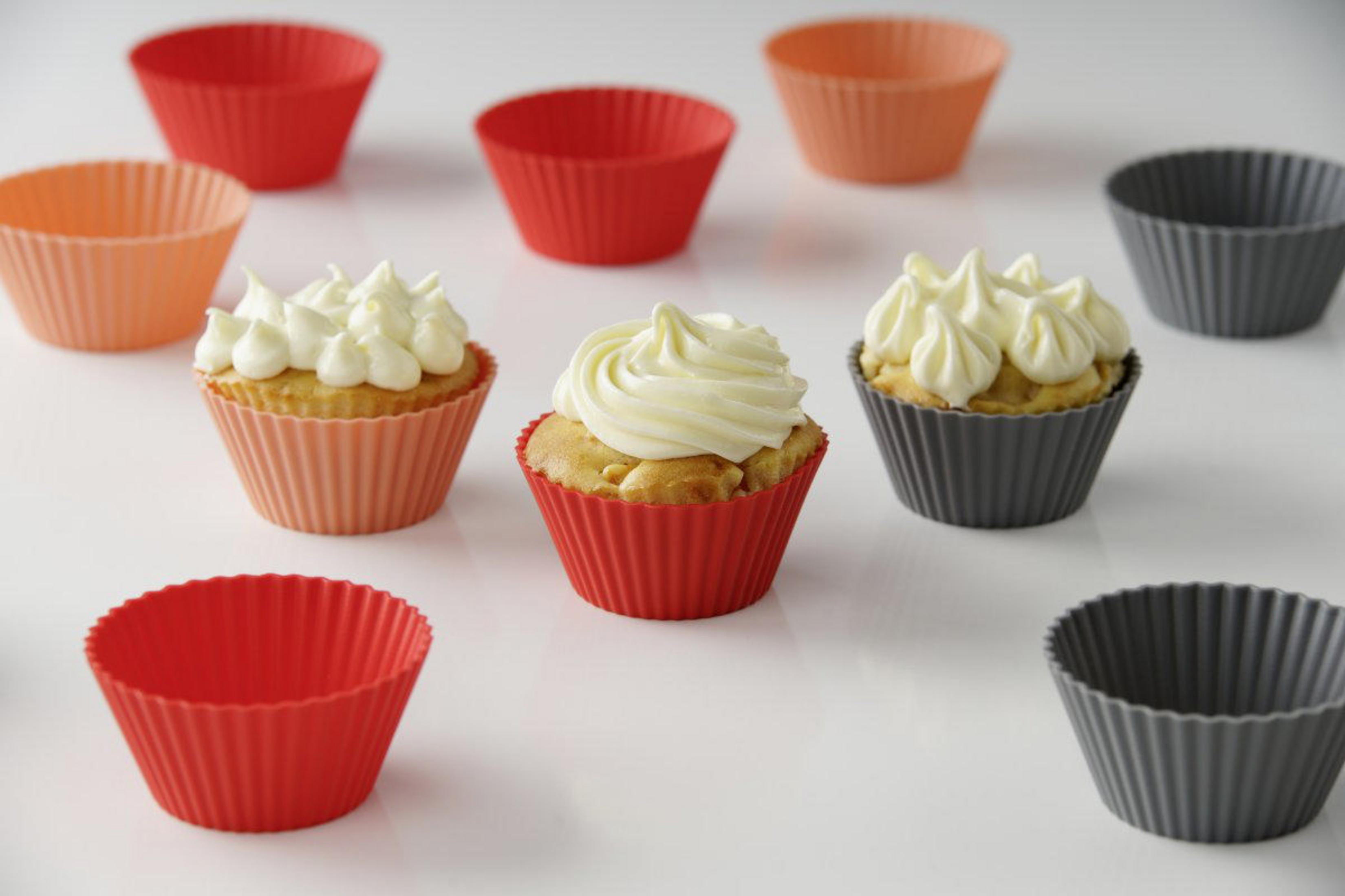 Cupcakes in roten, pfirsichfarbenen und grauen Silikonbechern. Einige haben weißes Frosting.