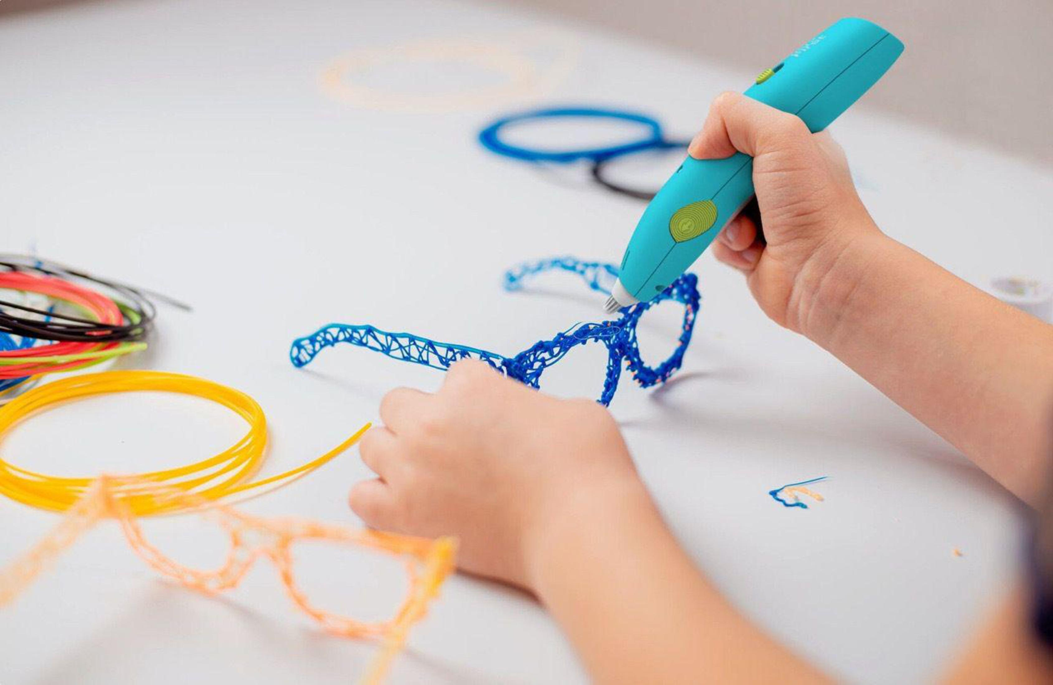 Un bambino usa una penna 3D per creare montature di occhiali blu. Sono visibili altri colori di filamento.