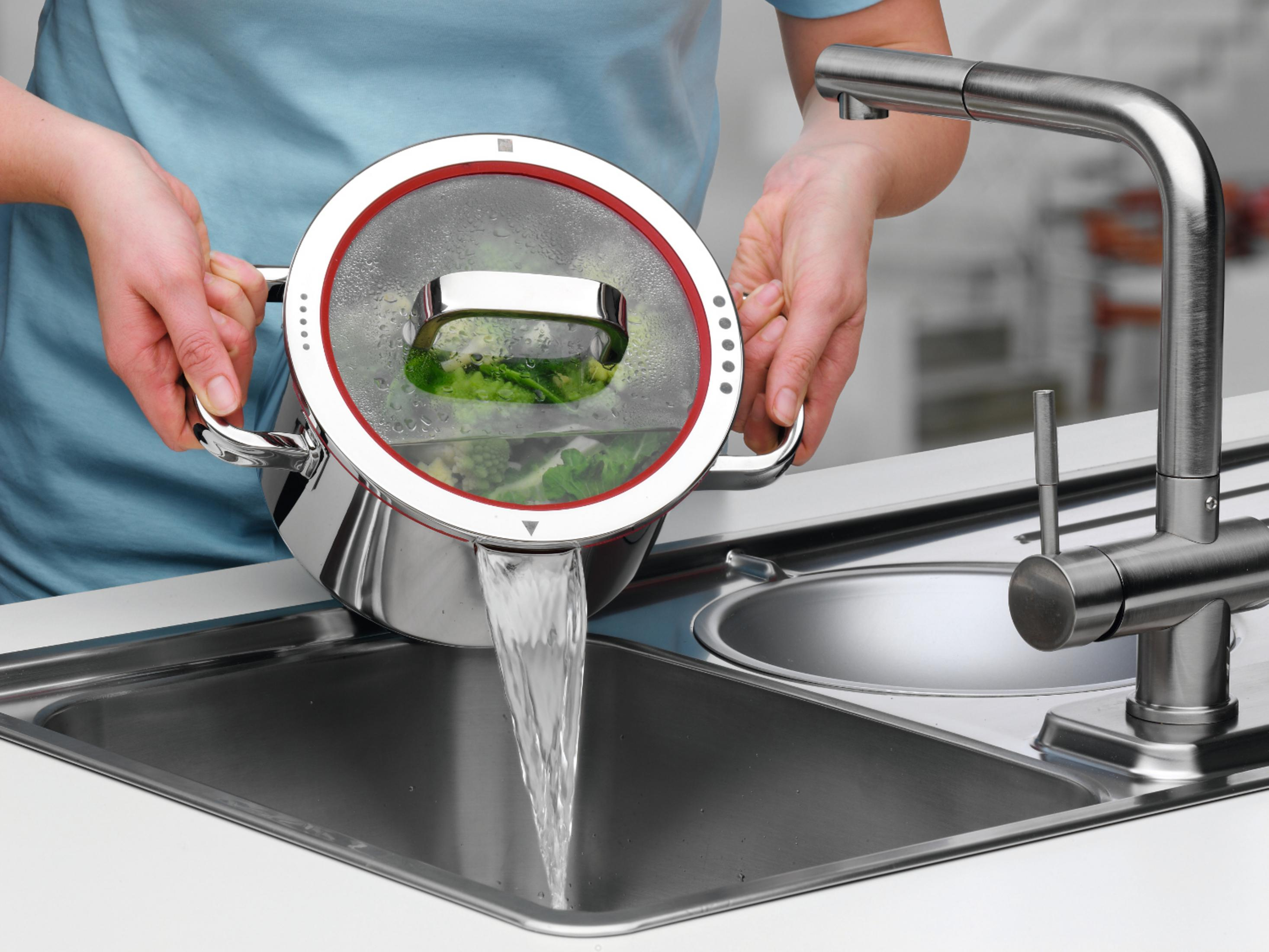 Hände, die Wasser aus einem Topf mit Brokkoli in ein Waschbecken gießen.