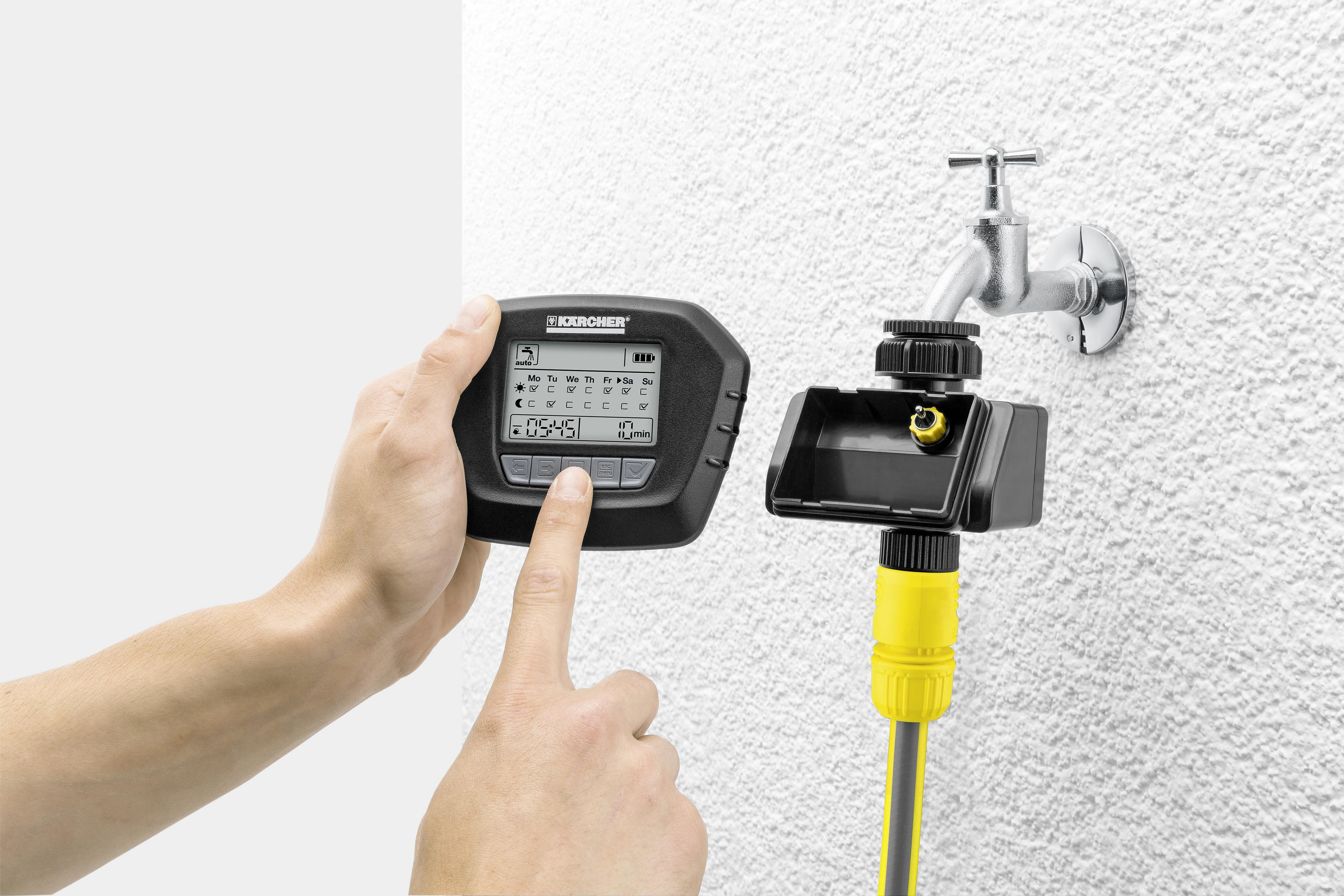 Hände einer Person, die einen digitalen Wasserzeitschalter neben einem Wasserhahn einstellen.