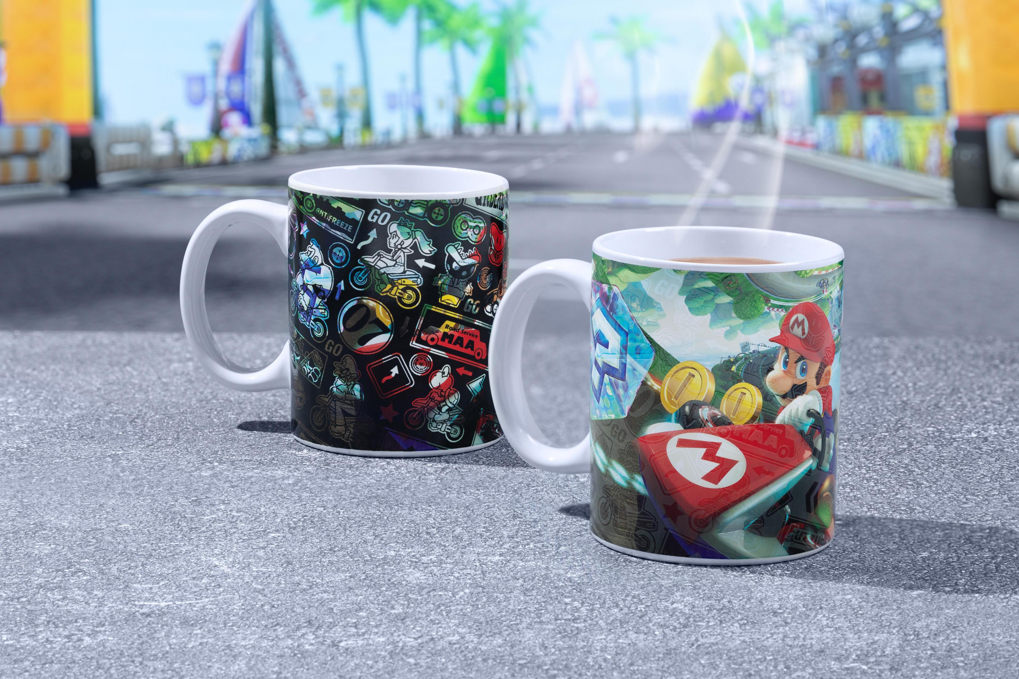 Zwei Tassen mit bunten Designs, eine mit Aufklebern und die andere mit einer Mario Kart Szene.