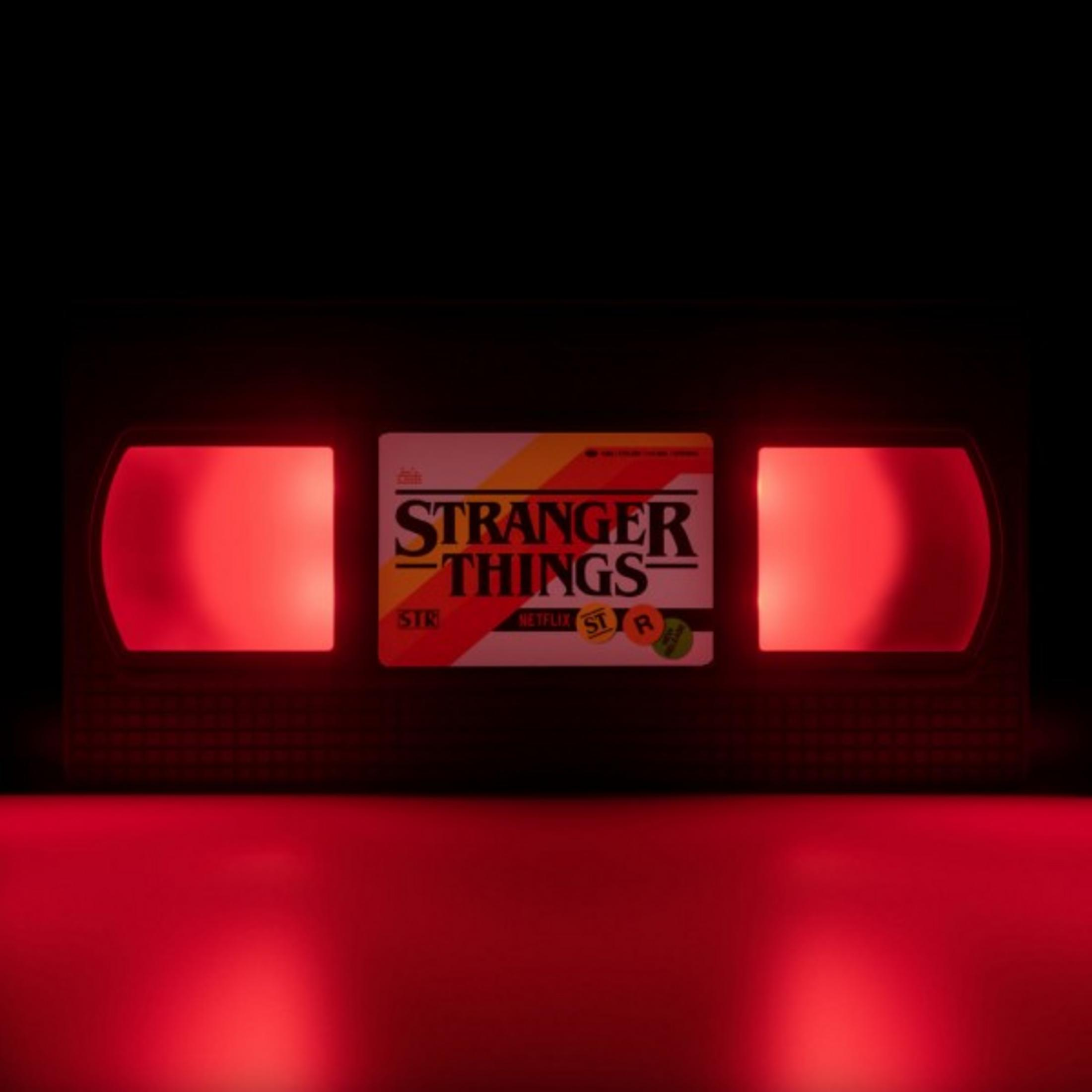 Eine Stranger Things VHS-Kassette leuchtet rot. Die Umgebung ist dunkel, unten leuchtet rotes Licht.