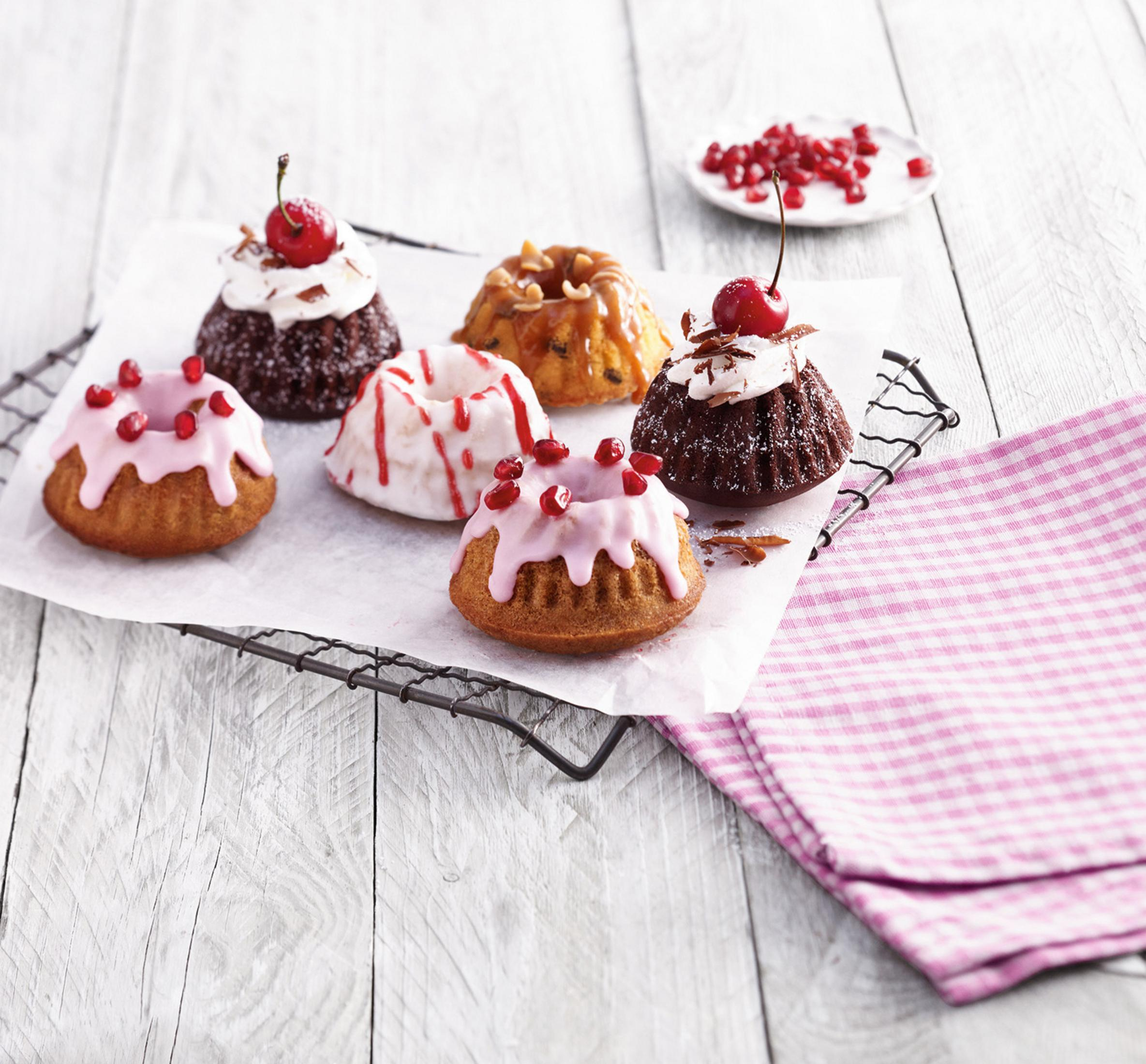 Kilka małych ciast bundt z różnymi polewami na białej powierzchni.