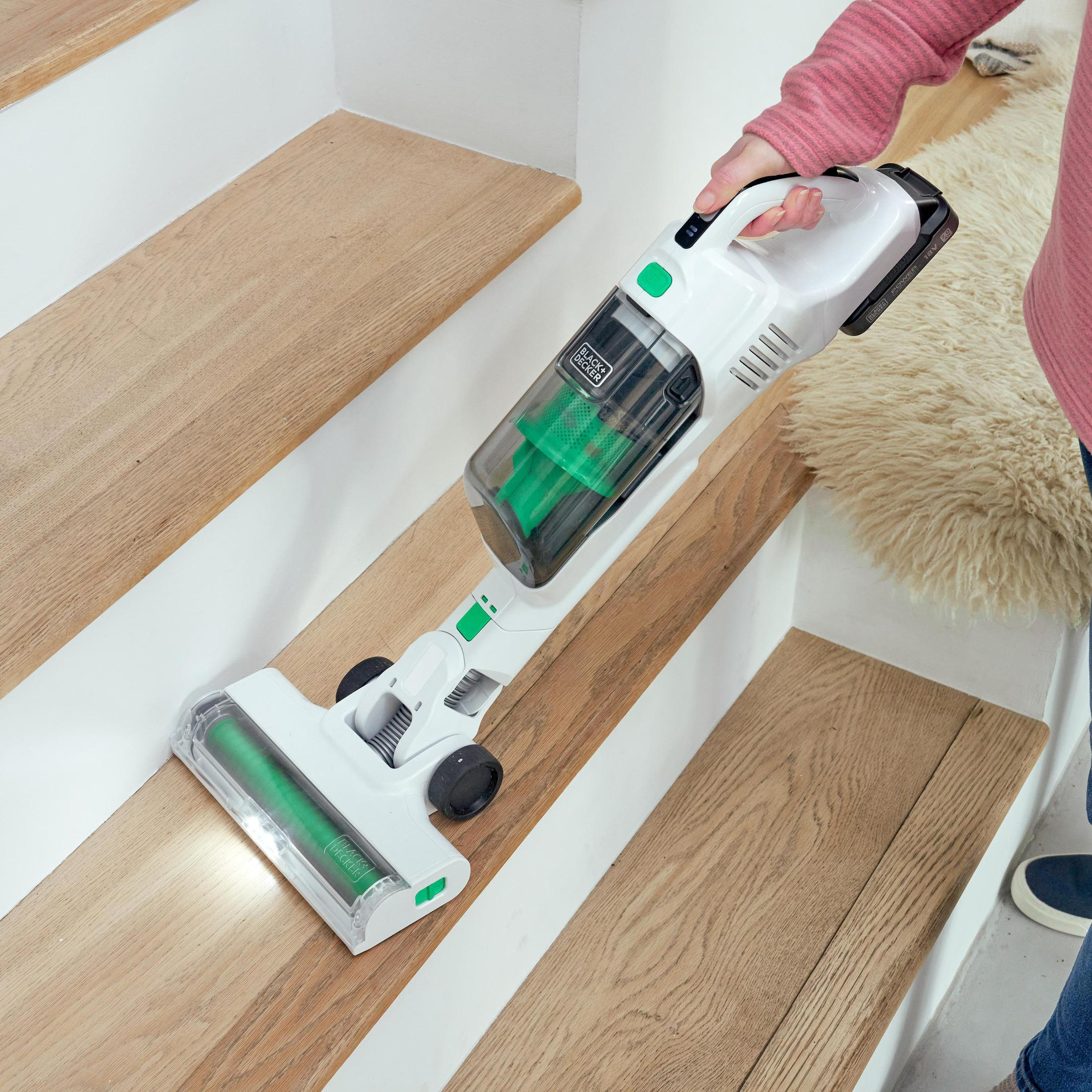 Una persona che aspira le scale con un aspirapolvere senza fili bianco e verde.