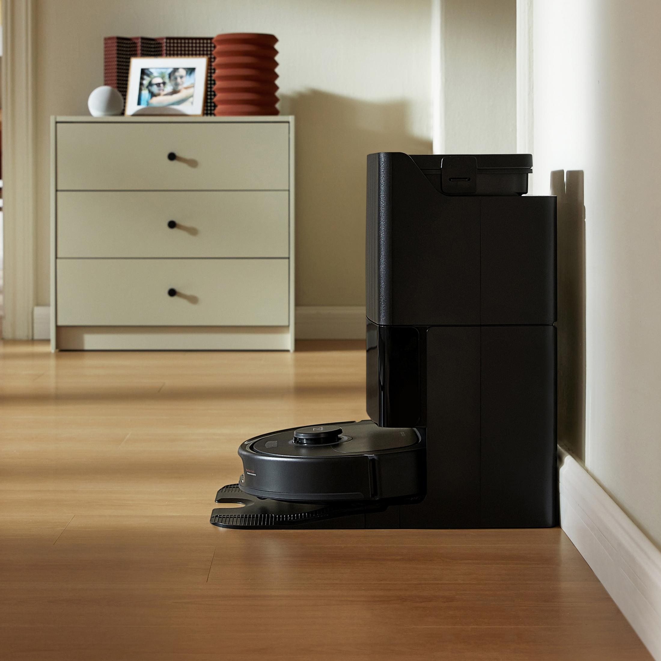 Stacja ładująca odkurzacza automatycznego obok ściany i komody.